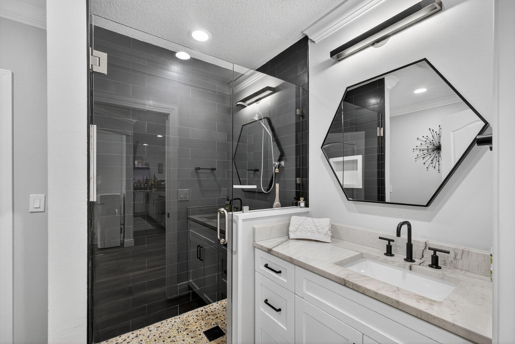 Bathroom featuring a vanity with stone countertop, rectangular undermount sink, and matte black widespread faucet, paired with a walk-in shower enclosed by glass and finished with dark tile and a mosaic-tiled floor
