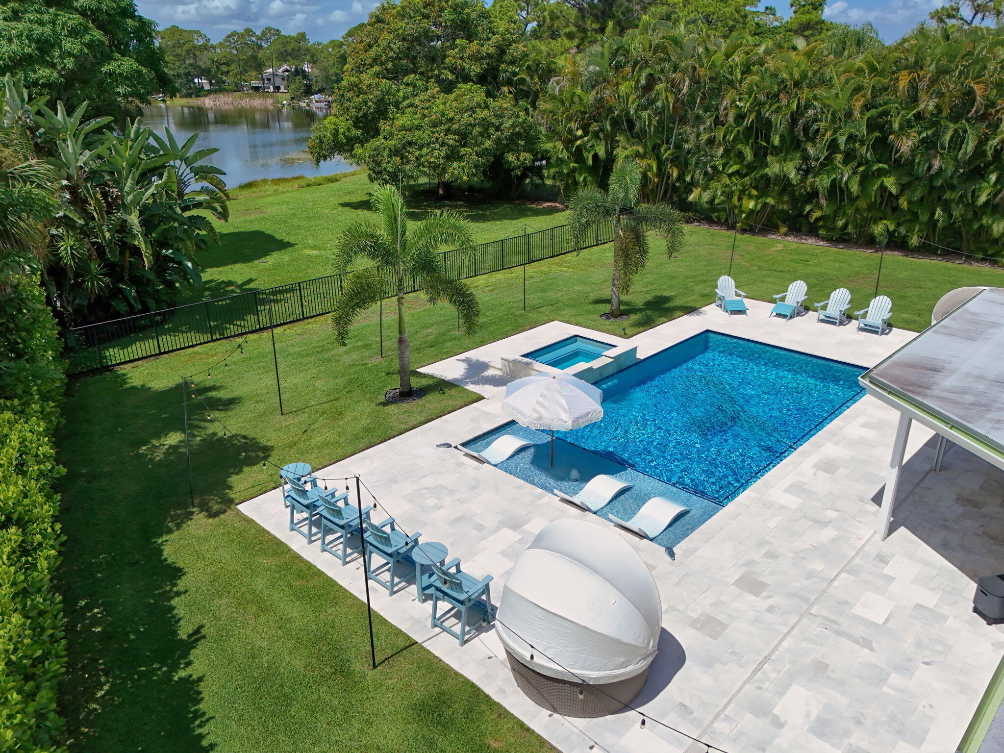 Backyard featuring an in-ground swimming pool with a tanning ledge, an integrated spa, stone-finish pool decking, and waterfront positioning