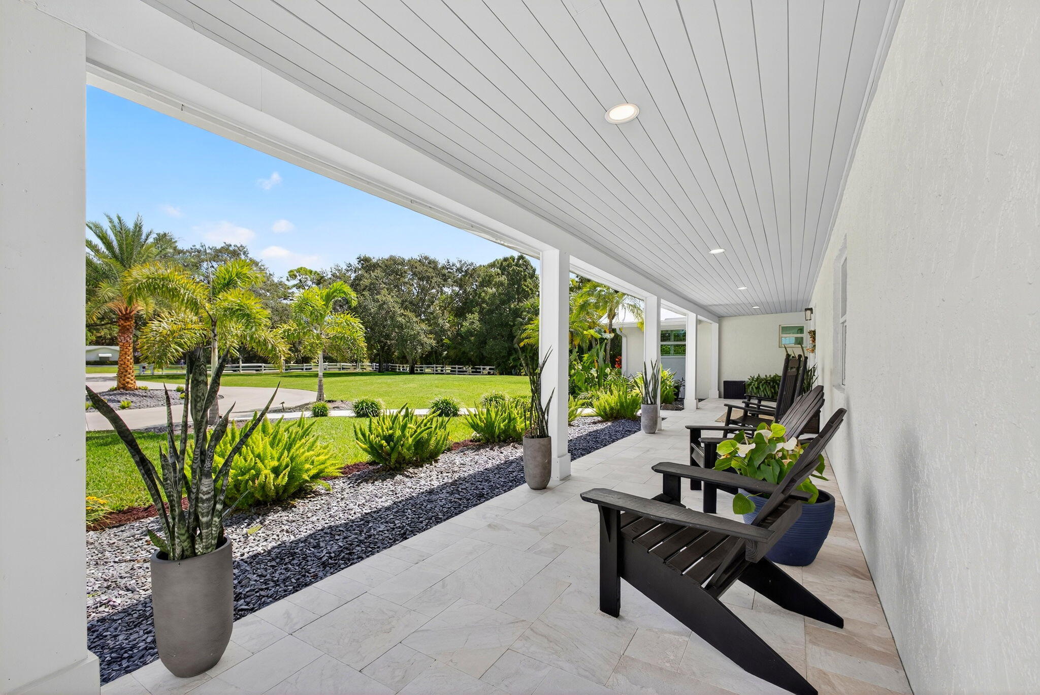 Covered porch featuring stone-finish flooring, recessed lighting, and a beadboard ceiling, overlooking a landscaped lawn with crushed stone borders