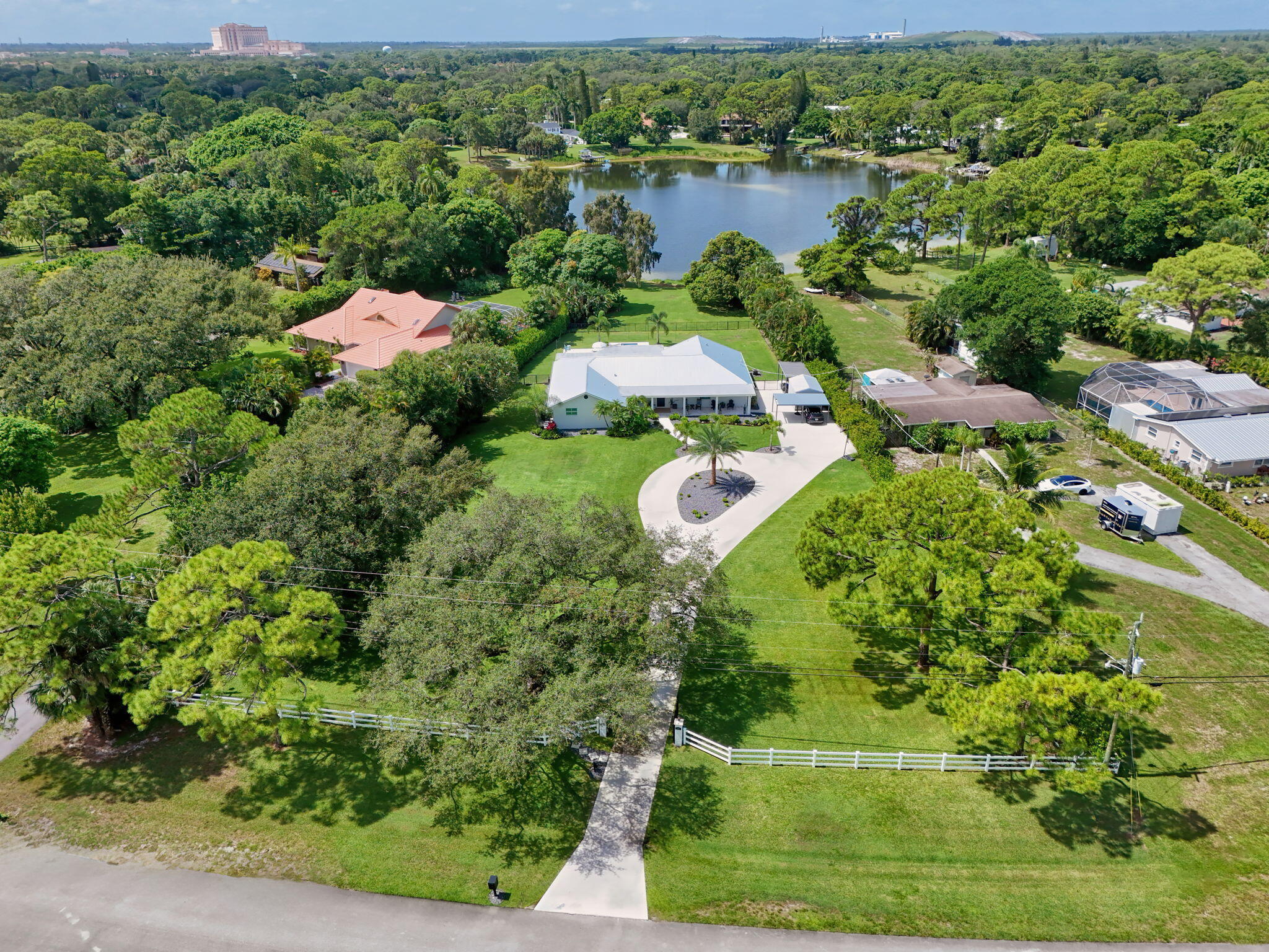 Aerial perspective of a sprawling lot featuring a gated entrance, expansive green space, mature trees, a curved concrete driveway, and direct water frontage