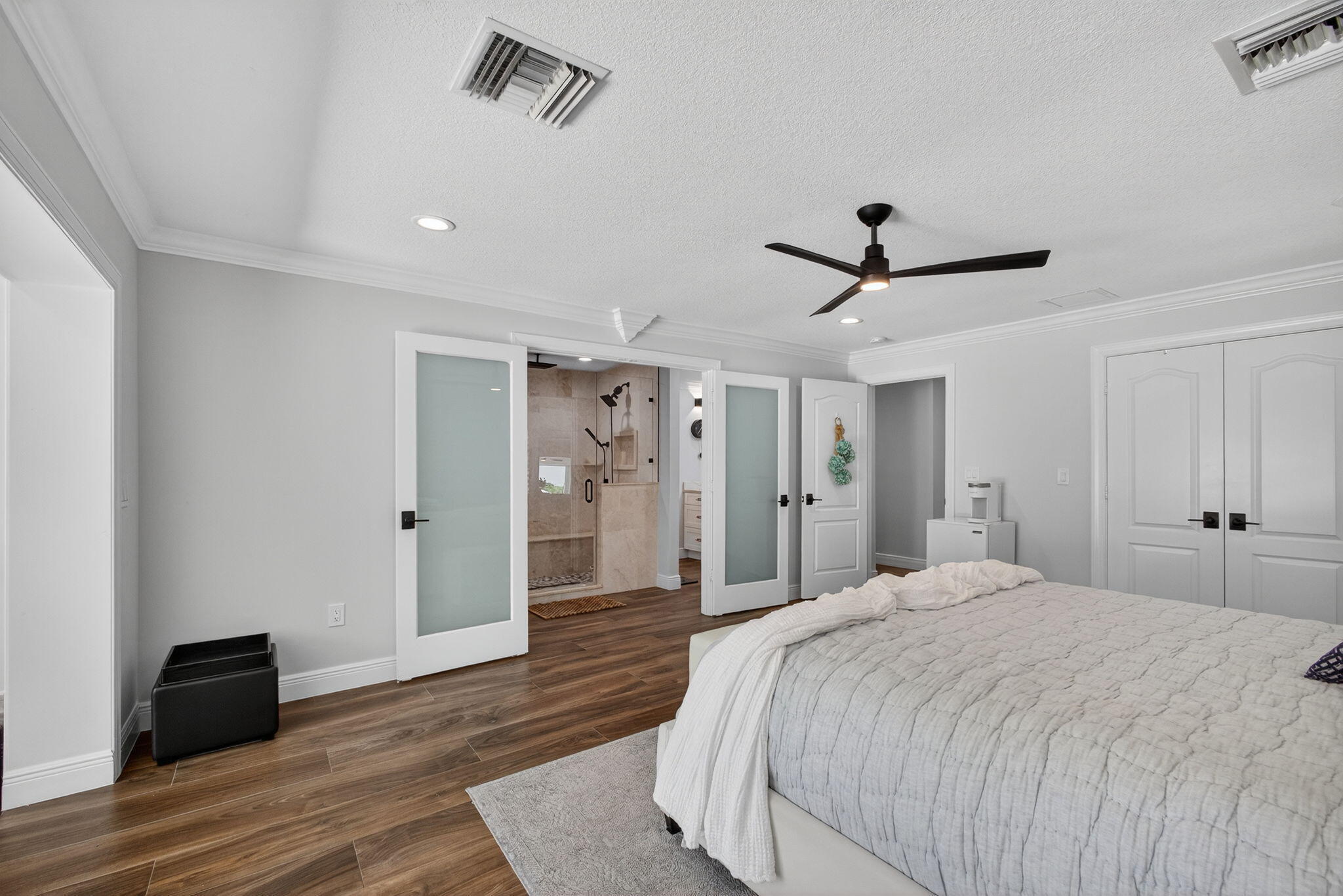 Wood-finish flooring, double frosted-glass interior doors, modern ceiling fan, and crown molding