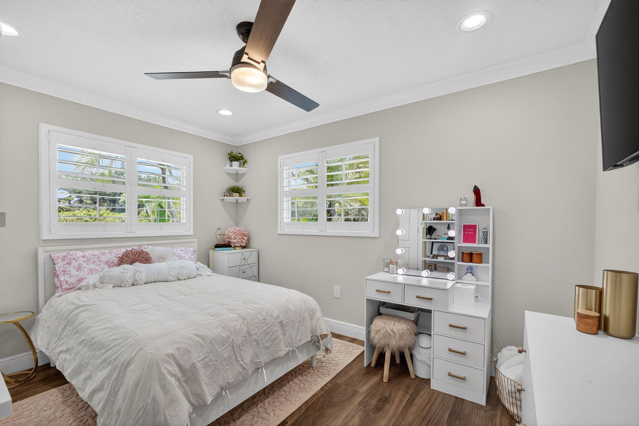 Room featuring wood-finish flooring, plantation shutters, crown molding, built-in corner shelving, and a multi-blade ceiling fan