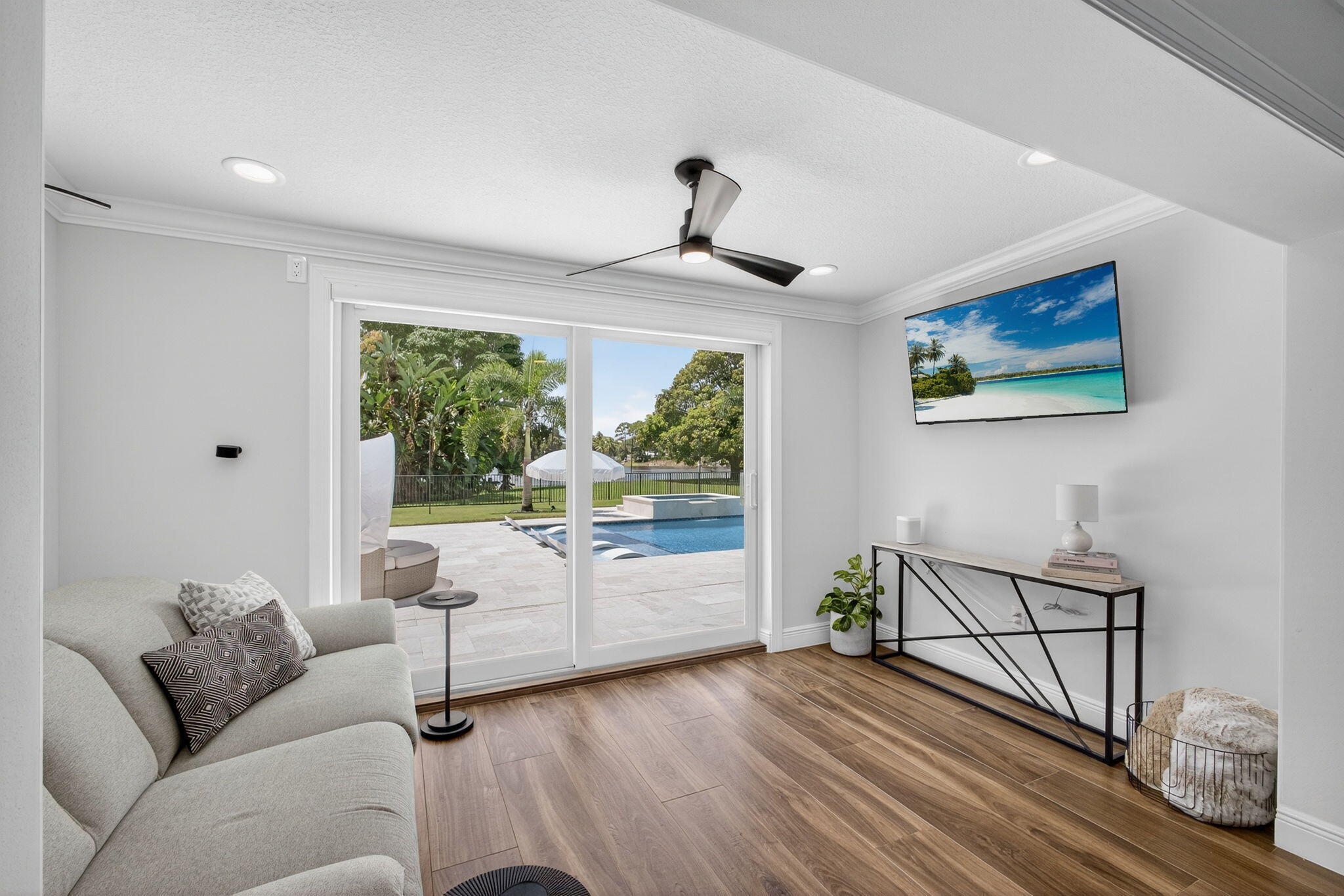 Wood-finish flooring, recessed lighting, modern three-blade ceiling fan, and sliding glass doors revealing a paved patio and swimming pool
