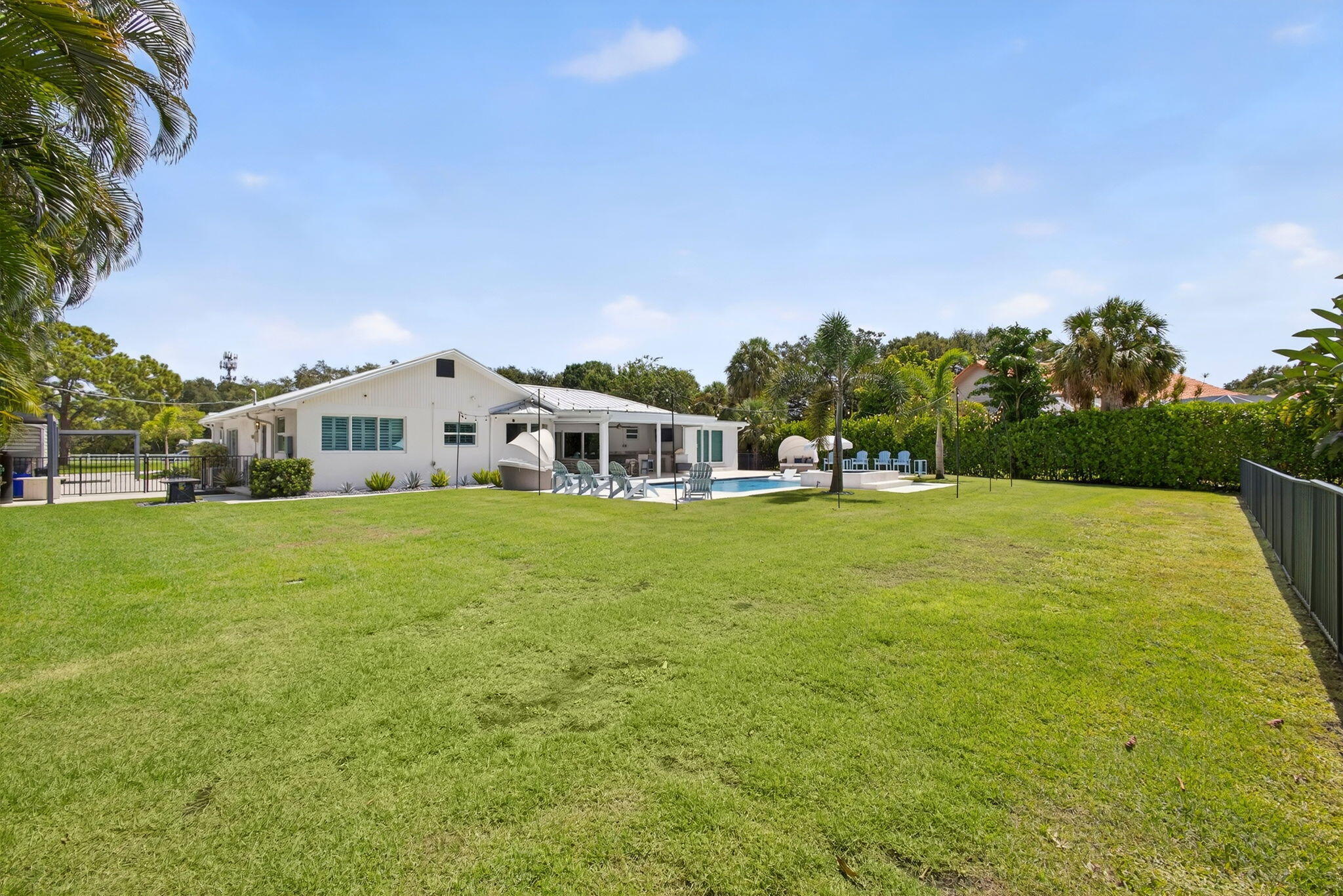 Expansive backyard featuring a large grass lawn, swimming pool, covered patio area, and mature perimeter landscaping