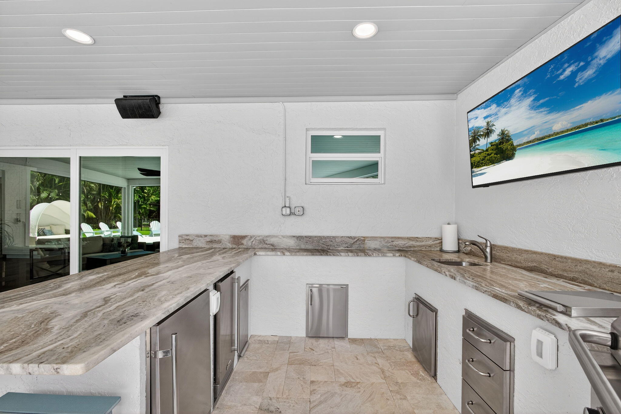 Outdoor kitchen featuring stone-finish countertops, stainless steel cabinetry, under-counter refrigeration, a built-in sink, and tile flooring