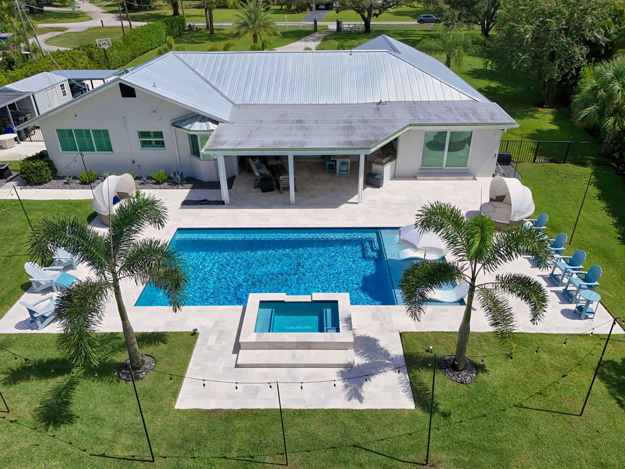 Aerial view featuring a swimming pool, integrated spa, covered patio, metal roof, and stone-finish pool deck