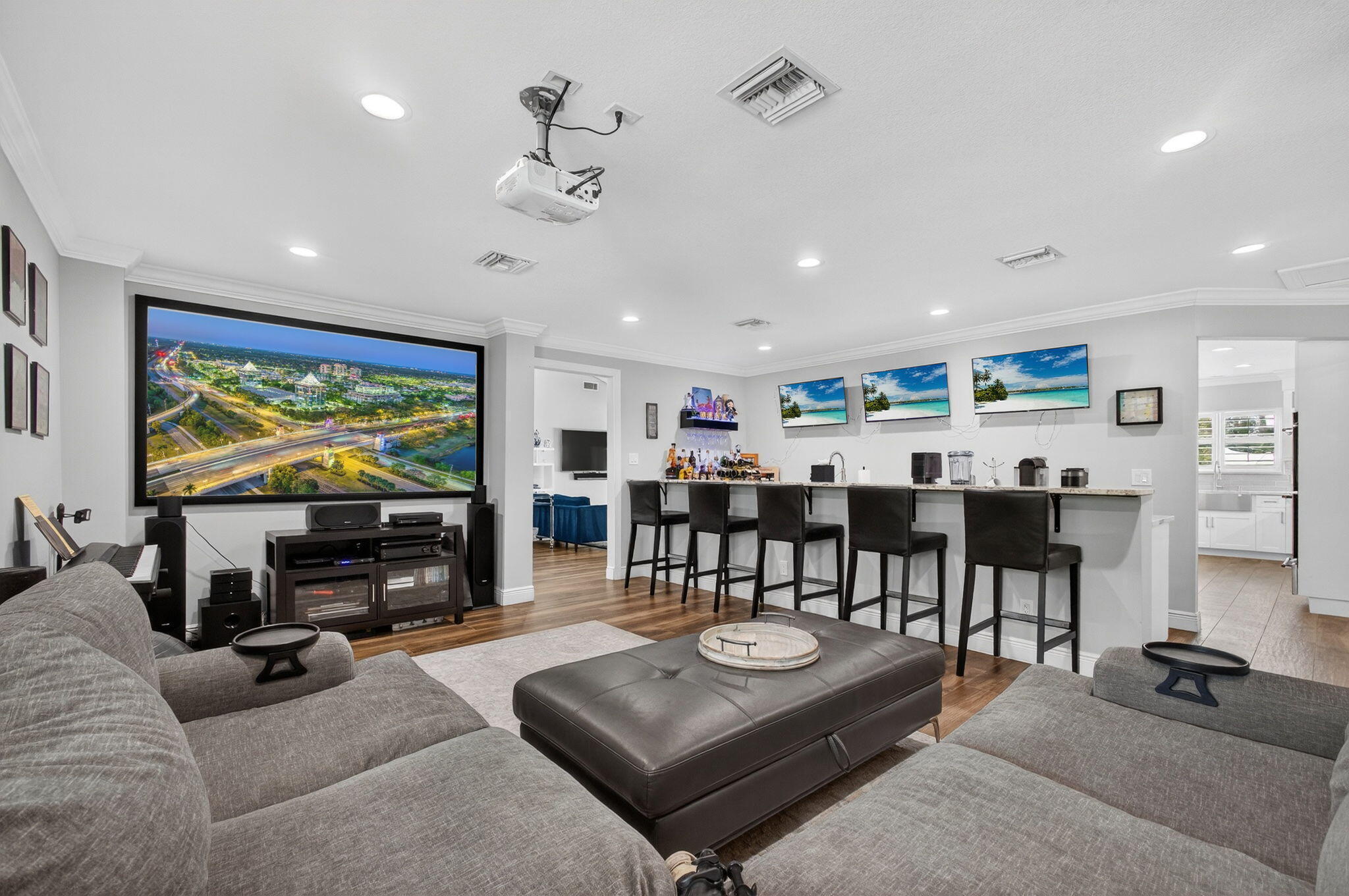 Custom entertainment space featuring a large-format projector screen, recessed ceiling lighting, wood-finish flooring, and a built-in wet bar with a countertop
