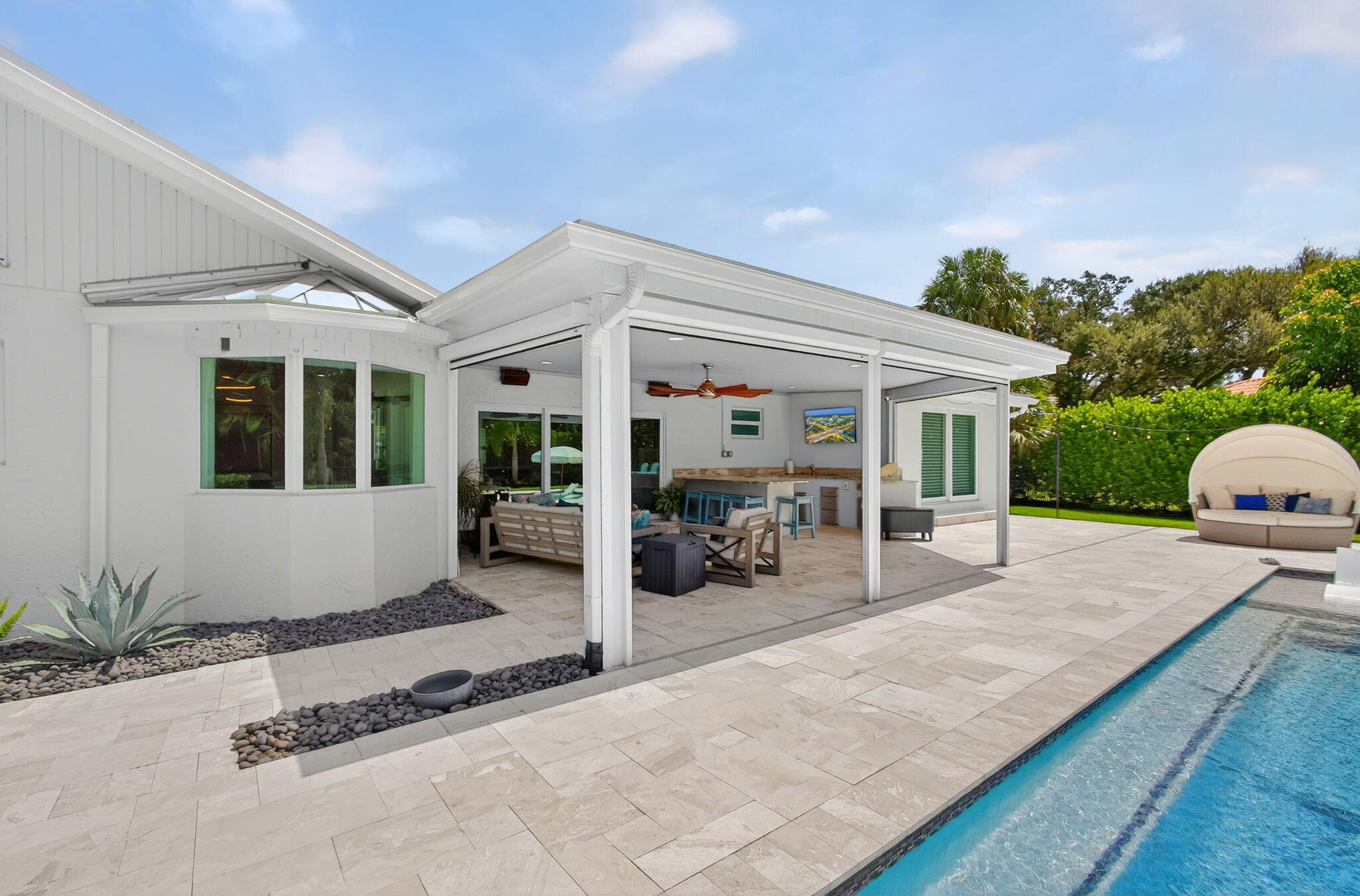 Covered patio with integrated outdoor kitchen, stone-finish tile hardscaping, and swimming pool