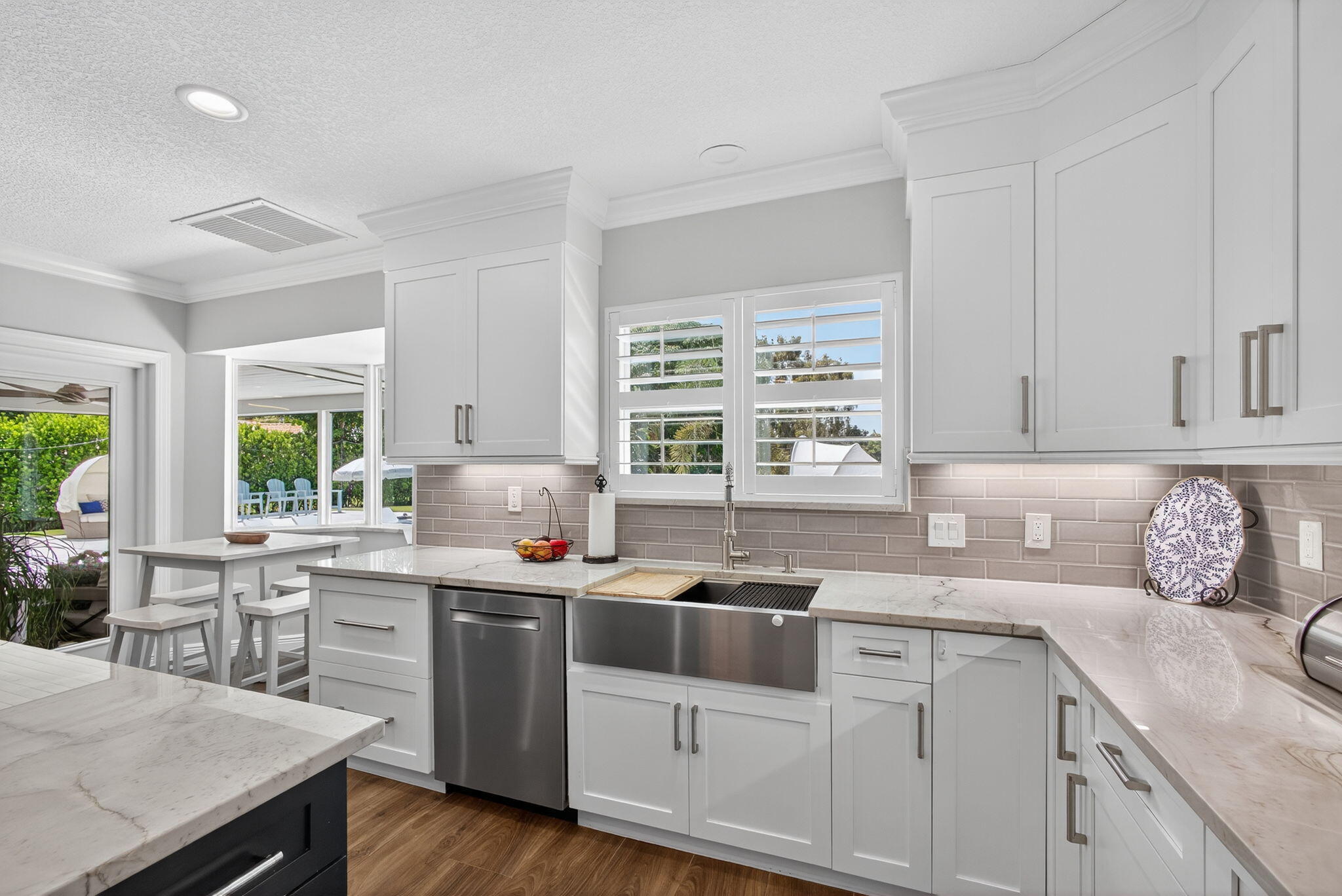 Kitchen featuring white shaker-style cabinetry, stone countertops, stainless steel farmhouse sink, subway tile backsplash, and recessed lighting