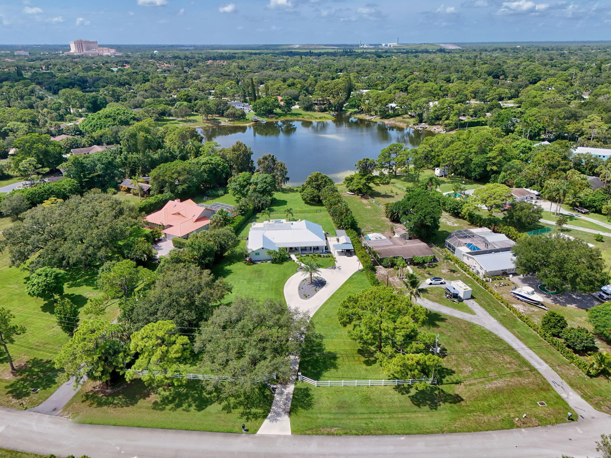 Aerial perspective of a sprawling property featuring a multi-gabled residence, a paved circular driveway, expansive manicured grounds, and direct frontage on a private lake