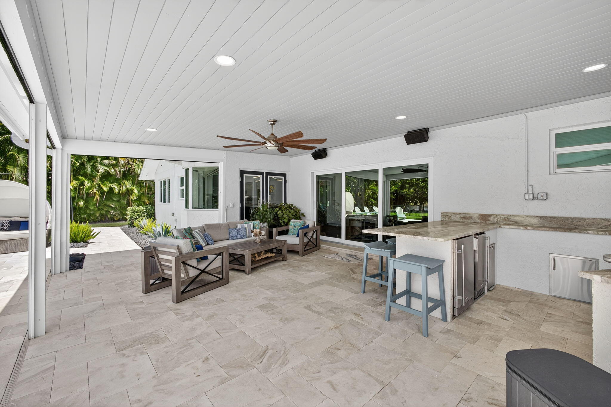 Covered outdoor patio featuring stone tile flooring, a built-in stone-topped bar with stainless steel appliances, recessed ceiling lighting, and a mounted ceiling fan