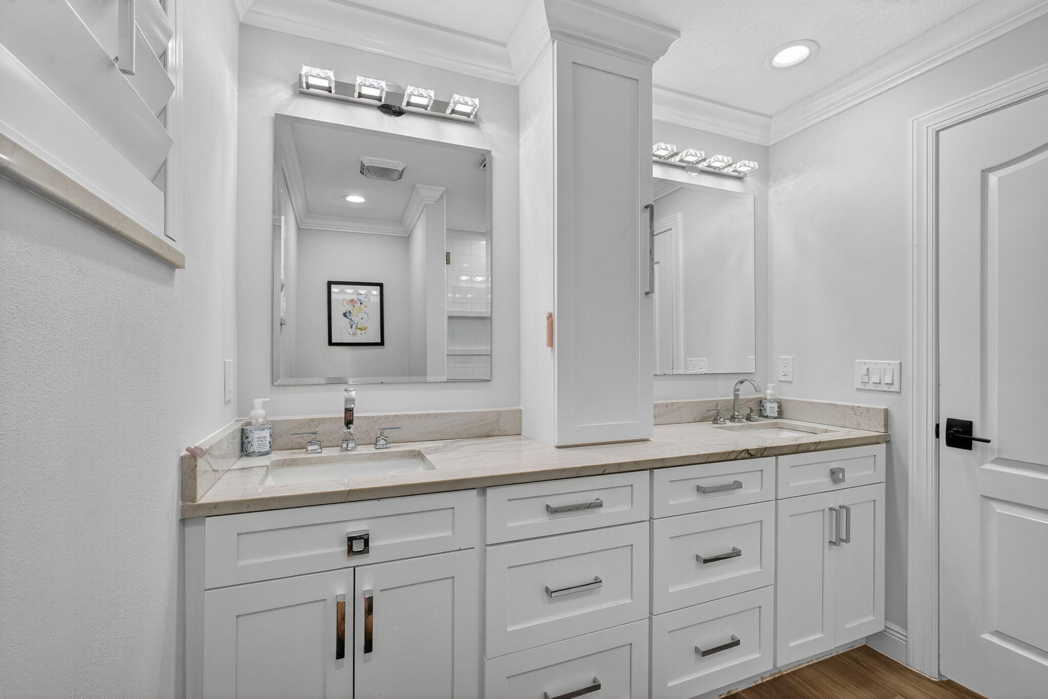Dual-sink vanity featuring white cabinetry, stone-finish countertops, undermount sinks, integrated linen tower, and contemporary metallic hardware