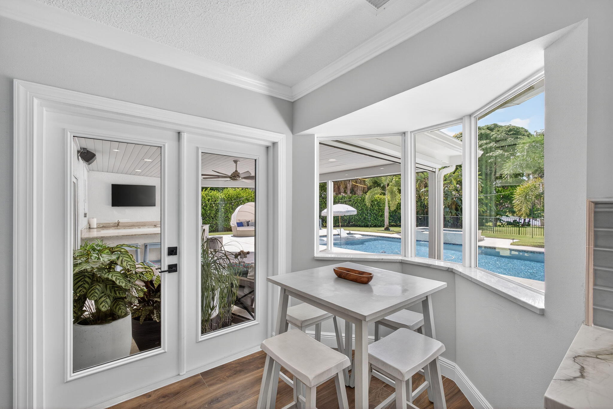 Bay window with stone-surfaced ledge, wood-finish flooring, and crown molding, featuring glass-paneled exterior doors