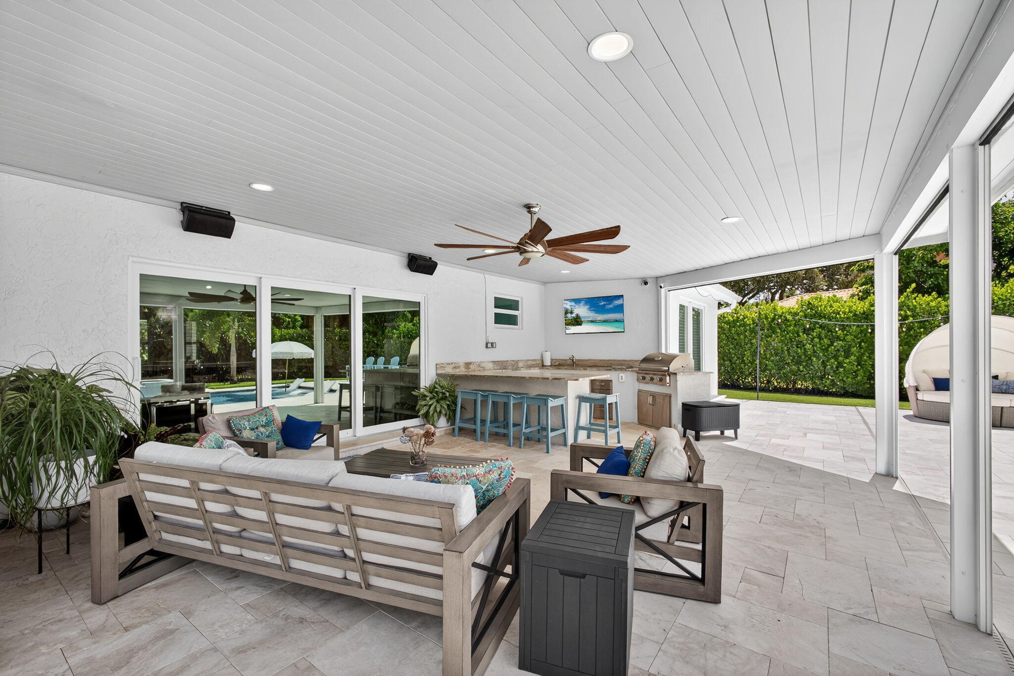 Covered outdoor living area featuring a tongue-and-groove ceiling, recessed lighting, ceiling fan, tile flooring, and a built-in outdoor kitchen with stone-finish countertops