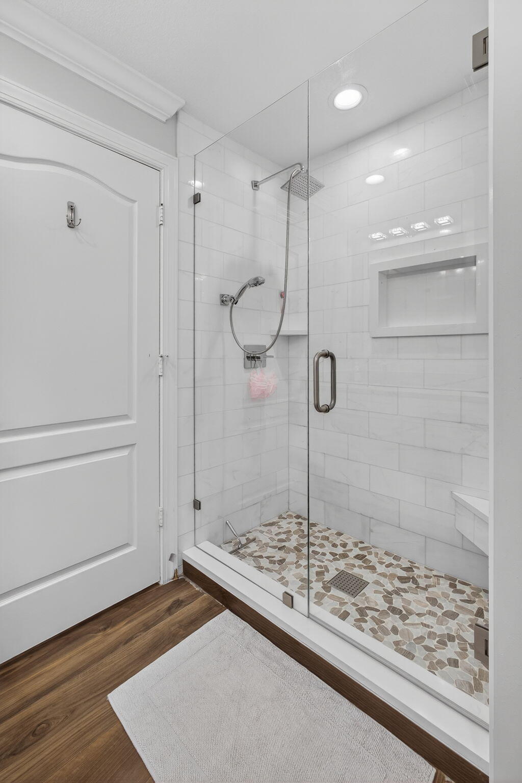 Walk-in shower featuring a glass enclosure, subway-style wall tile, a built-in recessed niche, a pebble-stone floor, and a handheld shower fixture