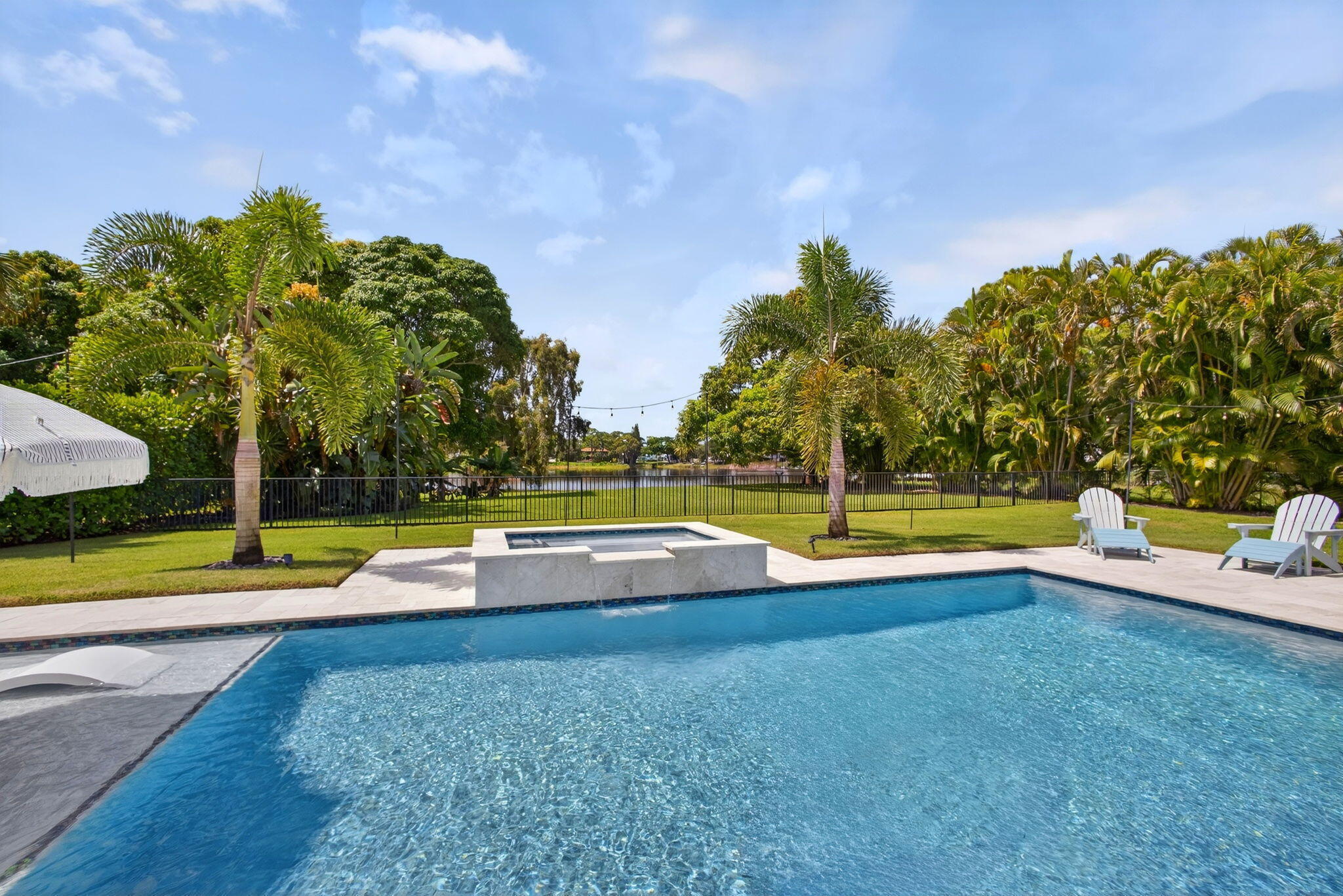 Backyard oasis featuring a swimming pool with a stone-finish spillover spa, expansive paver patio, manicured lawn, and mature perimeter landscaping
