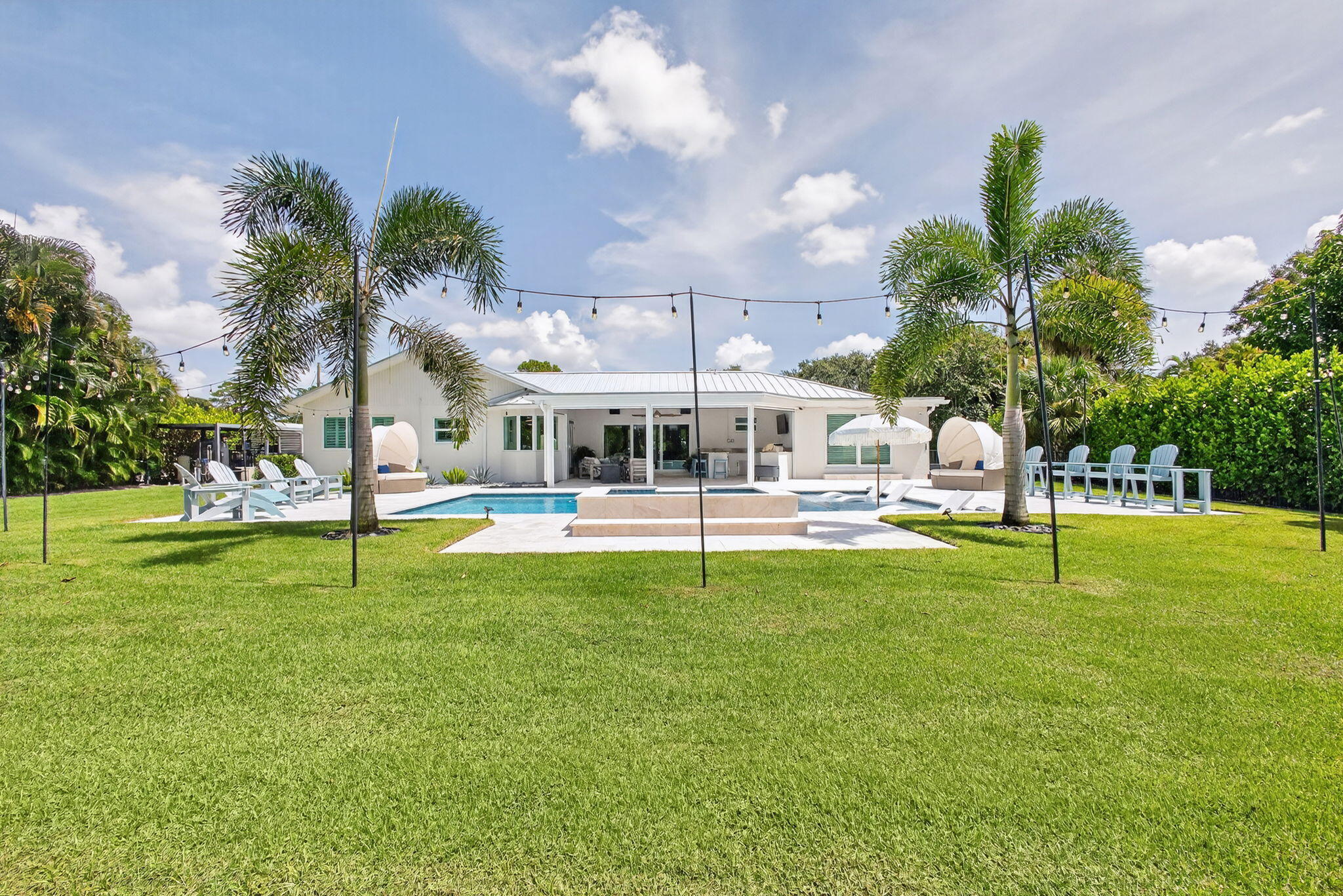 Expansive backyard featuring a swimming pool, stone-paver patio, covered porch, and mature palm trees