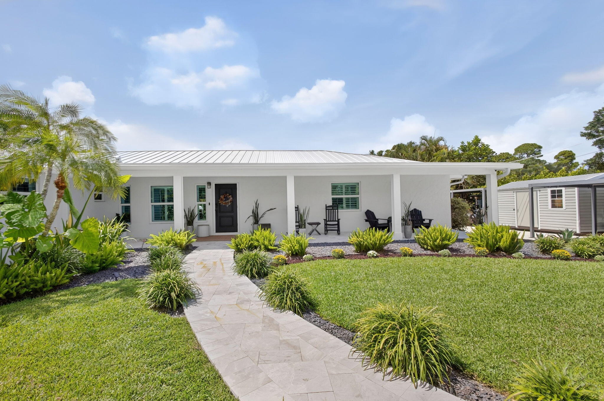 Single-story residence featuring a metal roof, expansive front porch, stone paver walkway, and manicured landscaping