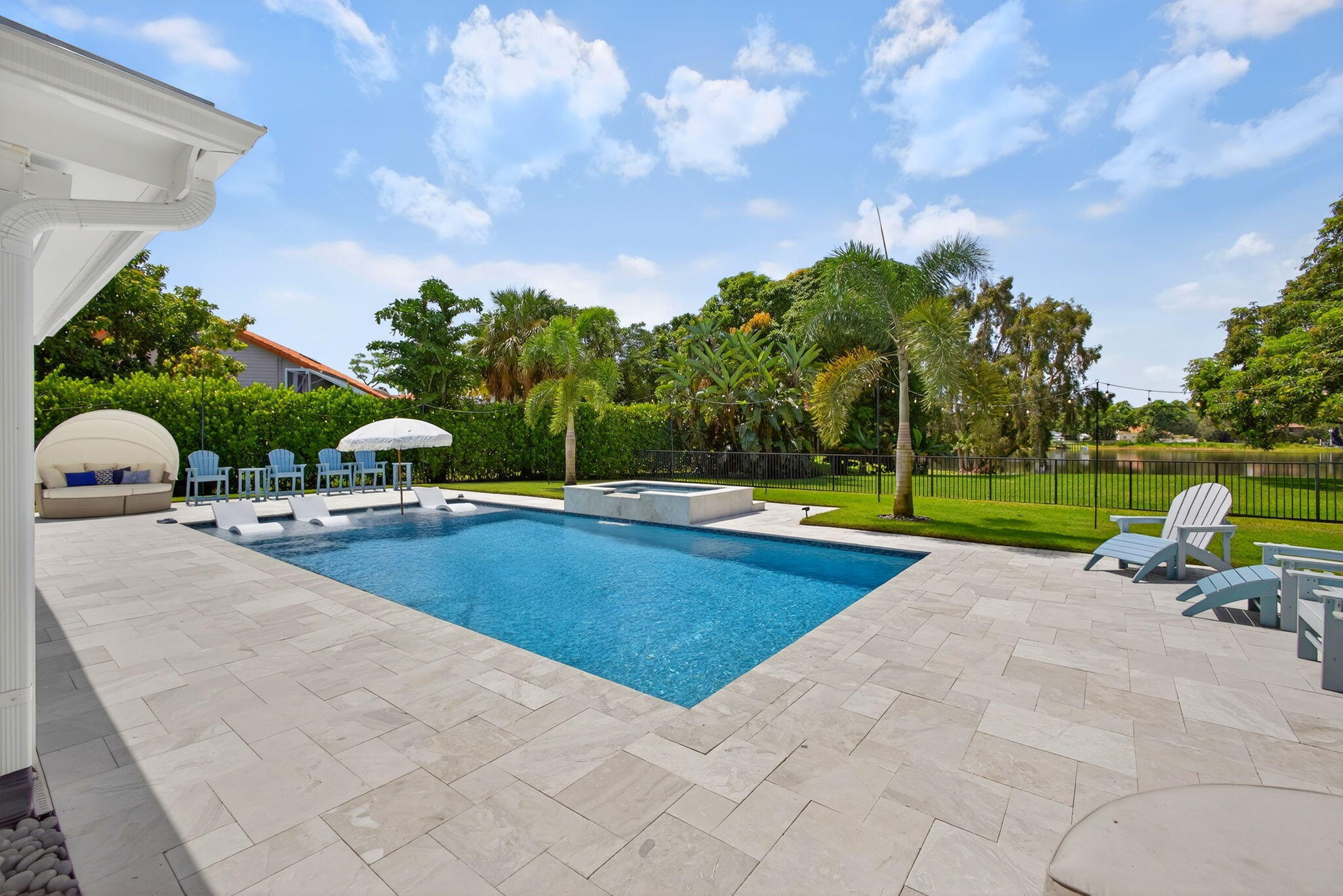 Private backyard featuring a swimming pool with a built-in spa, expansive stone paver patio, manicured lawn, and perimeter fencing