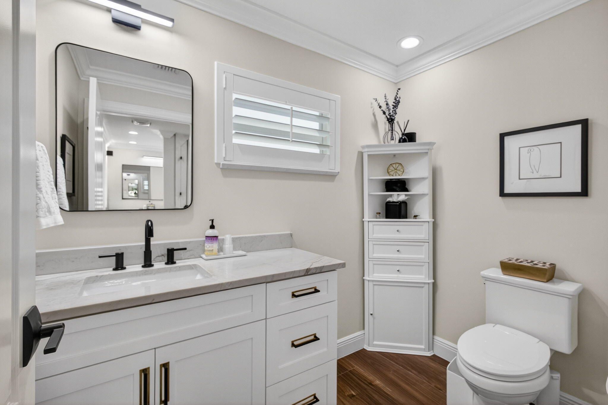 White vanity with stone countertop, matte black widespread faucet, rectangular undermount sink, built-in corner cabinetry, and wood-finish flooring