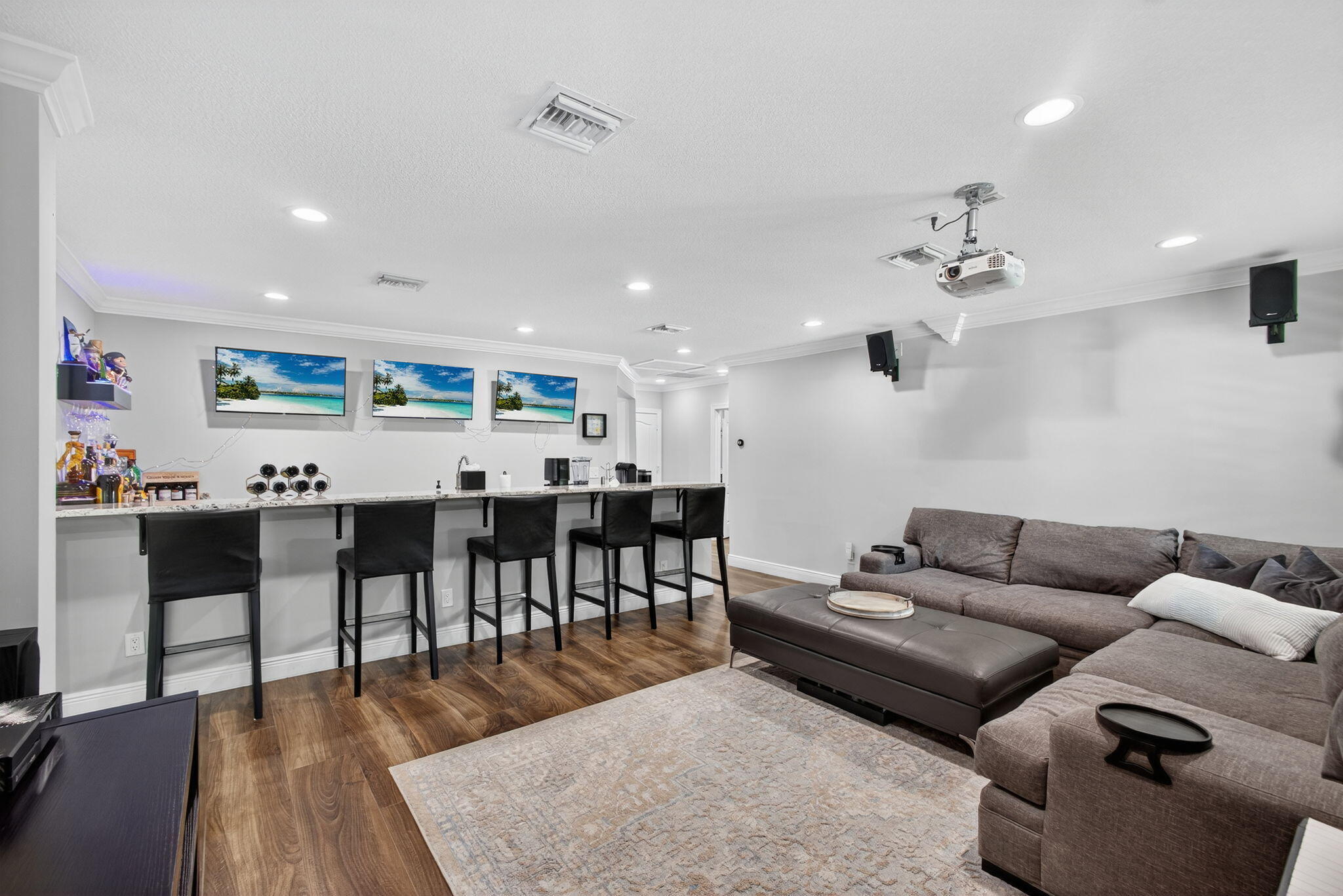 Built-in wet bar featuring a stone-surface countertop, recessed lighting, wood-finish flooring, mounted projector, and ceiling-mounted speakers