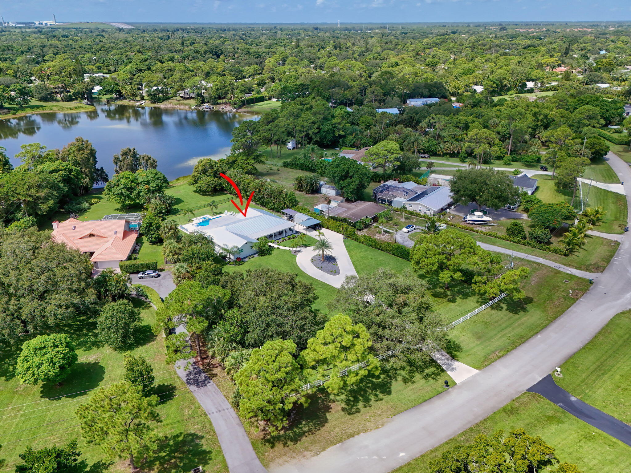 Aerial perspective featuring a waterfront property with an in-ground swimming pool, expansive lawn, mature landscaping, and a paved circular driveway