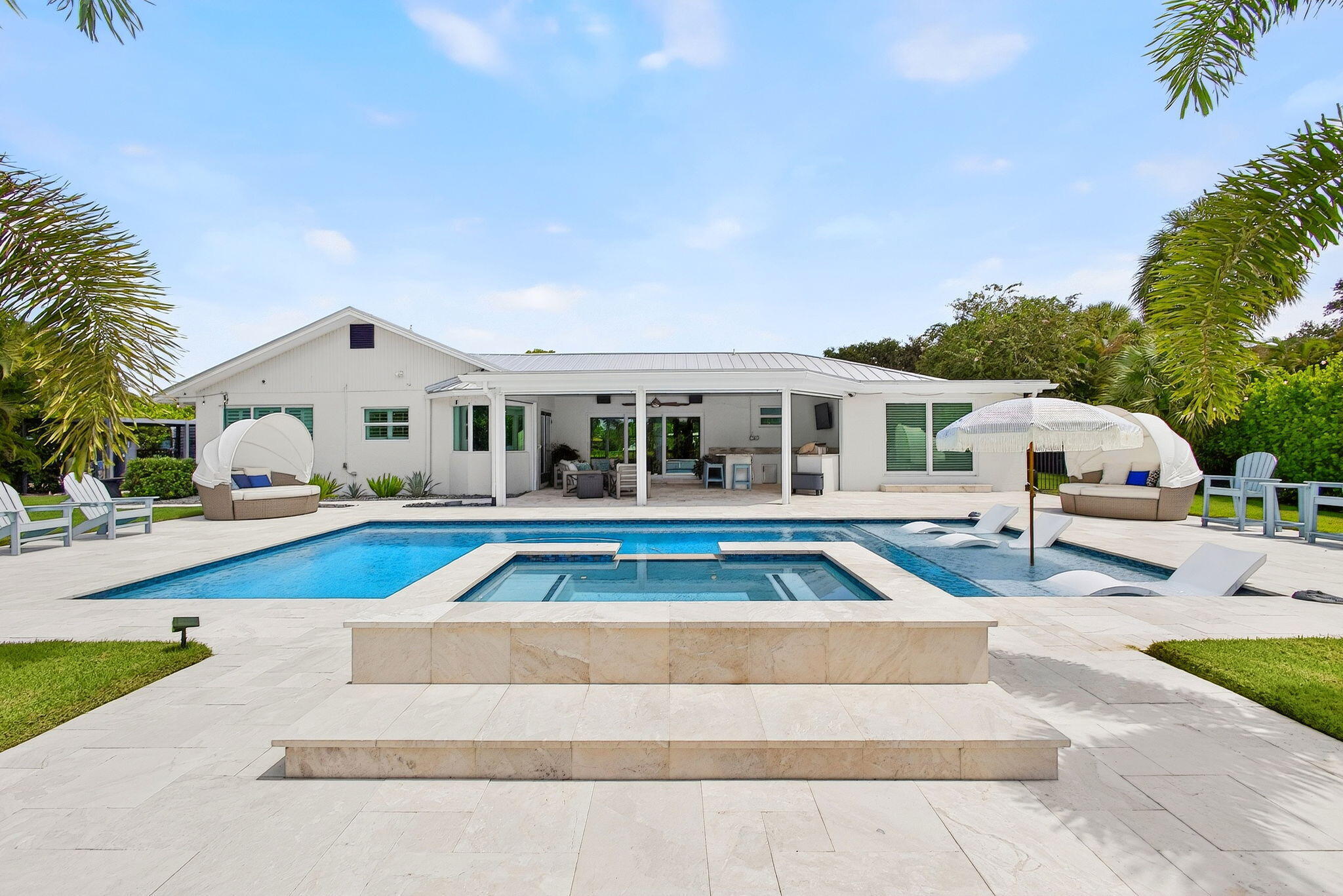 Backyard featuring a heated in-ground pool with integrated spa, sun shelf, light-toned stone pool deck, and a covered patio
