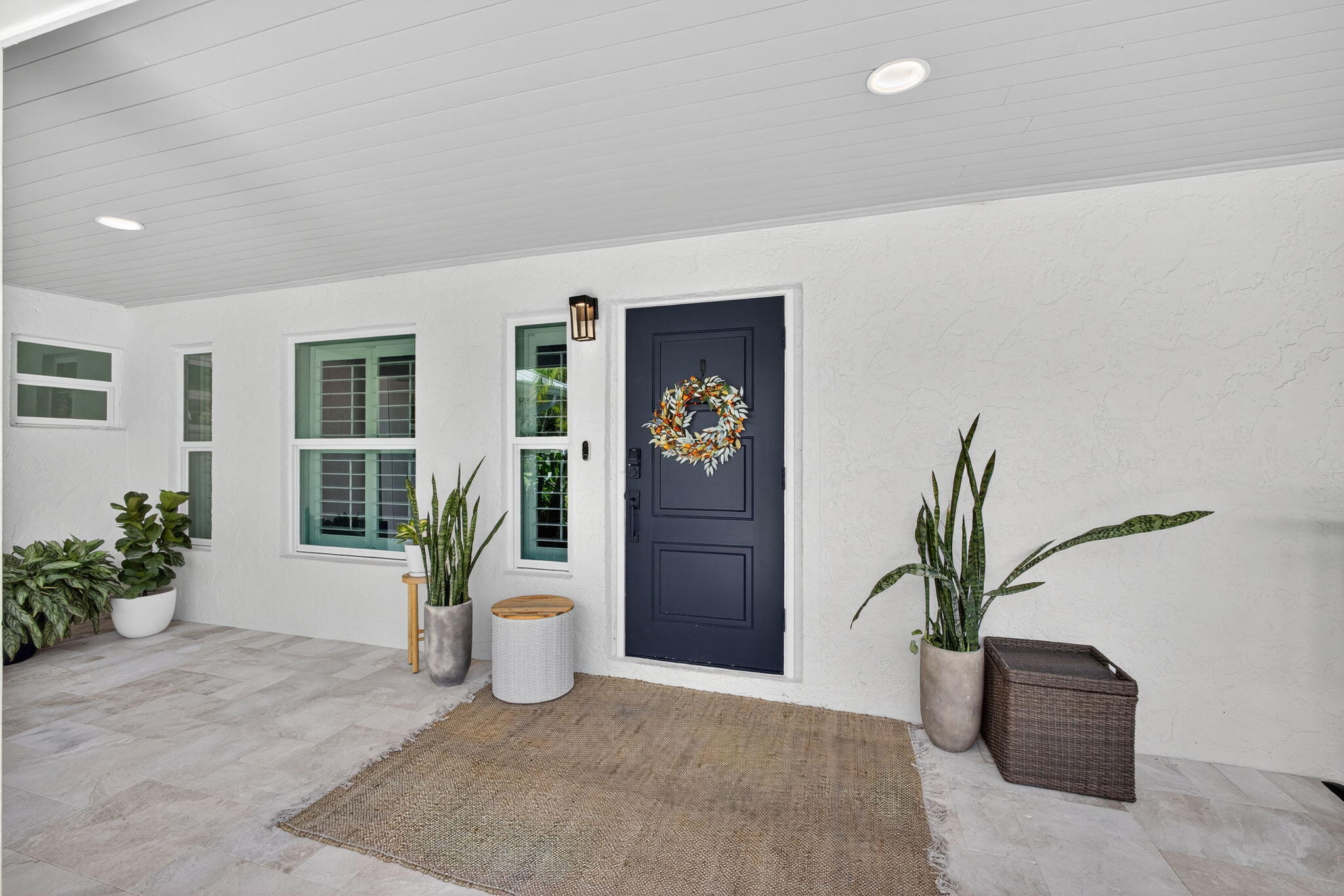 Covered entryway featuring large-format tile flooring, a solid panel front door, recessed lighting, and white stucco exterior finish