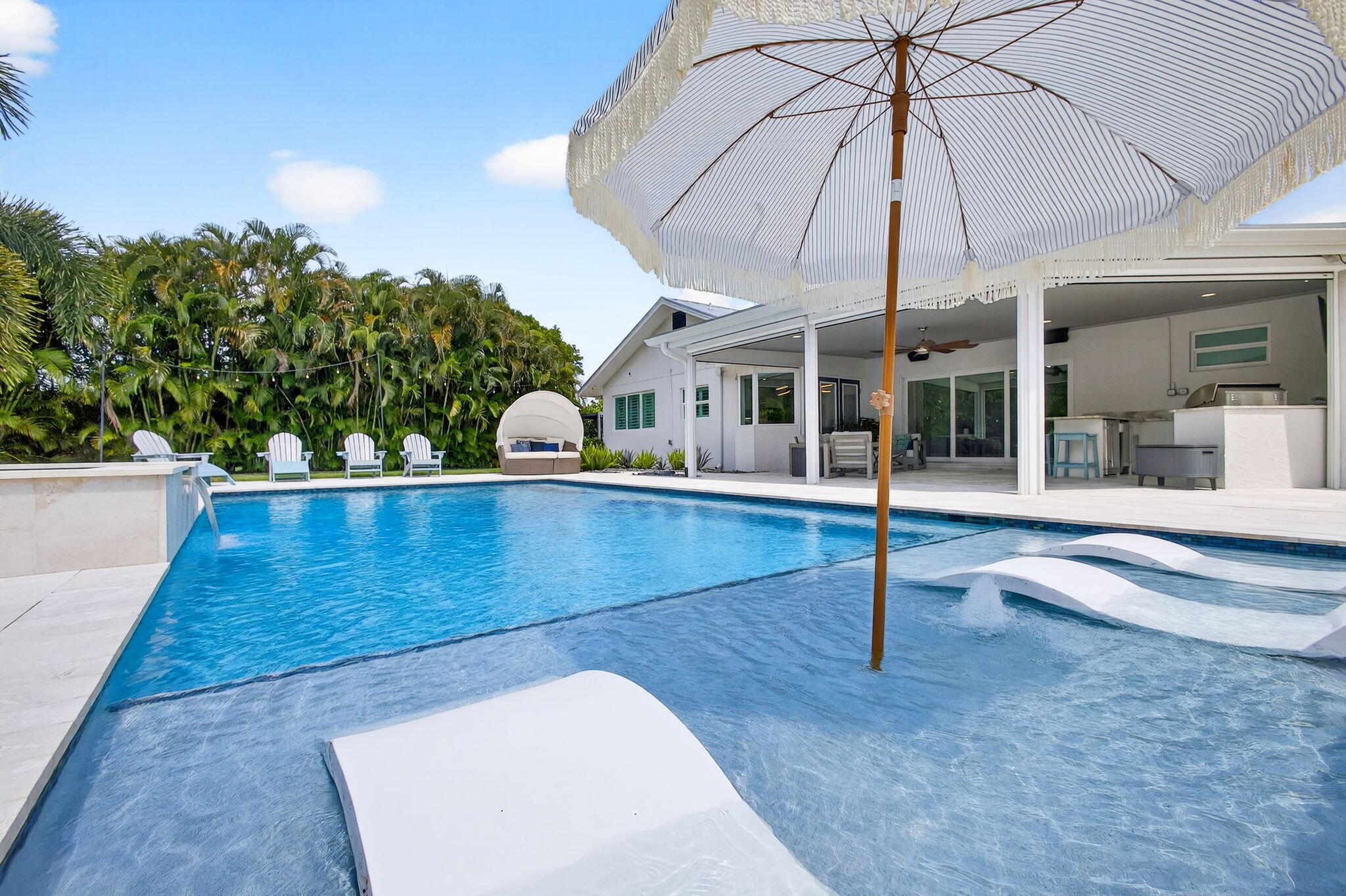 Swimming pool featuring a sun shelf with water fountains and stone surround tiling, paired with an expansive covered outdoor living area and built-in exterior kitchen
