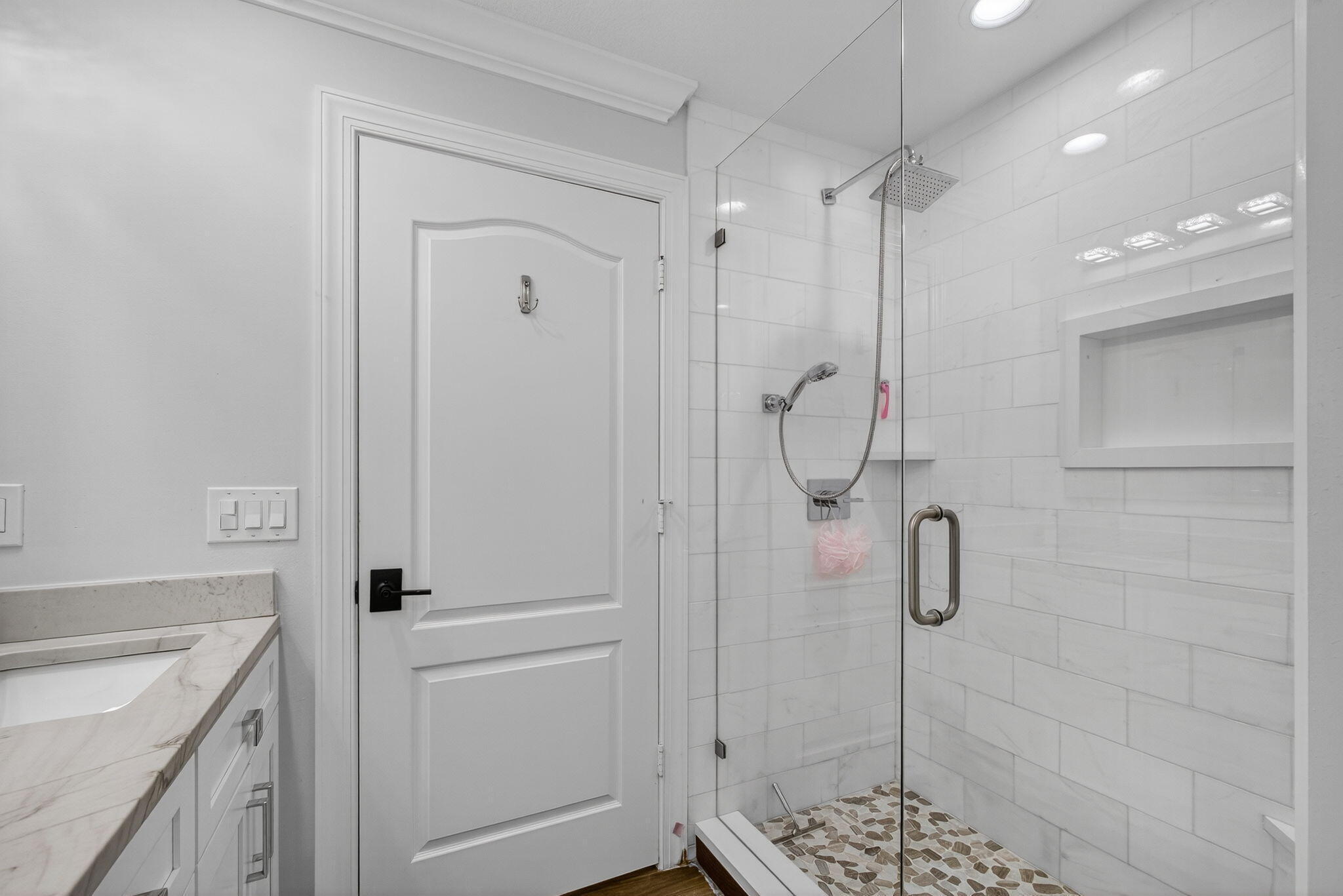Bathroom featuring a walk-in shower with glass enclosure, subway tile surround, built-in recessed shelf, stone-finish flooring, and vanity with stone countertop