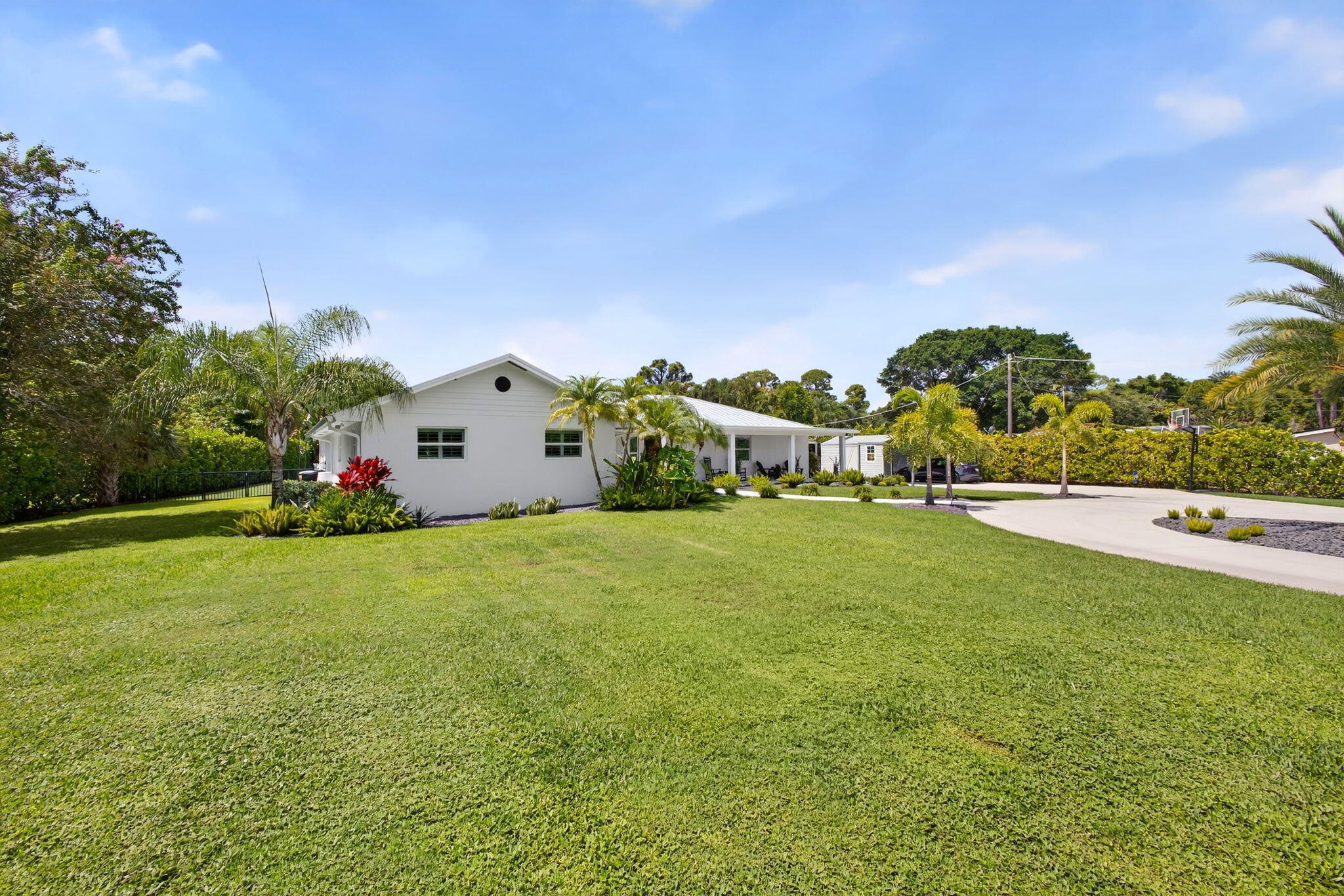 Single-story residence featuring a painted masonry exterior, a circular concrete driveway, and expansive manicured lawn with mature palm trees