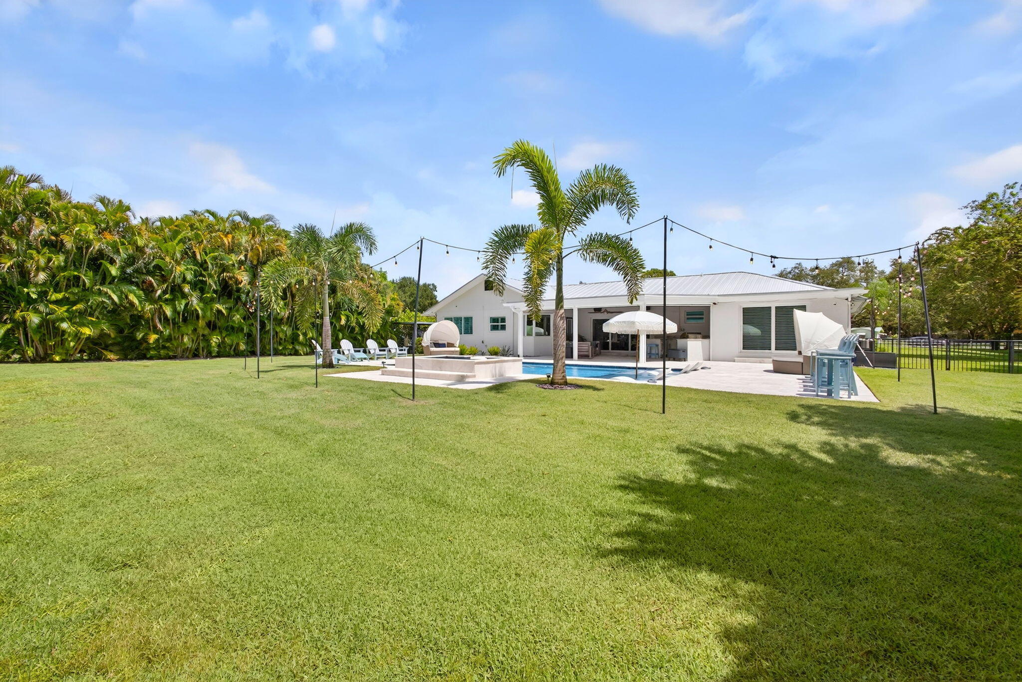 Expansive backyard featuring a grass lawn, in-ground swimming pool, stone-paver patio, and mature perimeter landscaping