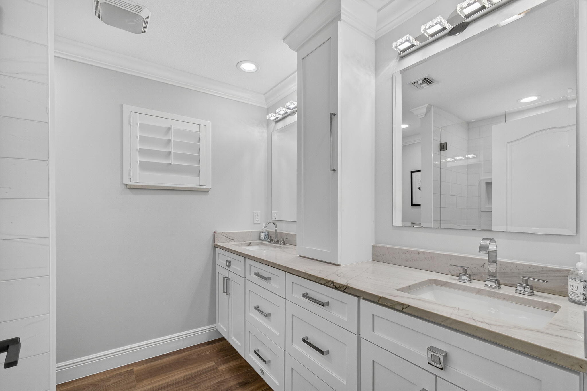 Dual-vanity cabinetry with shaker-style white doors, stone-finish countertops, undermount rectangular sinks, chrome widespread faucets, and integrated tower storage