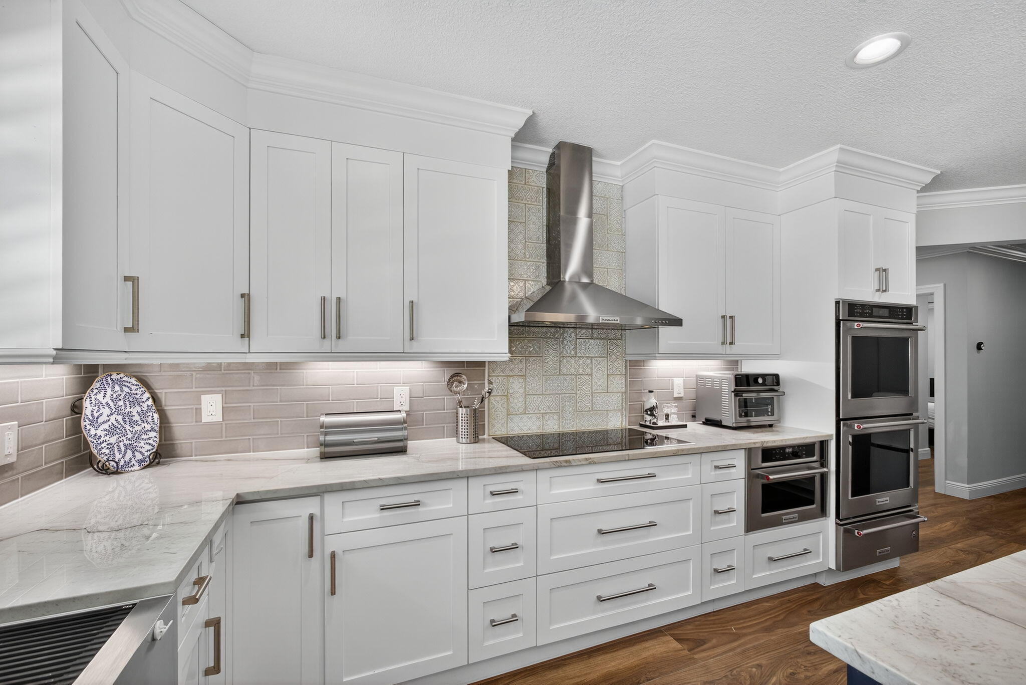 Kitchen featuring white shaker-style cabinetry, stone-surface countertops, subway tile backsplash, stainless steel built-in double wall ovens, and wood-finish flooring