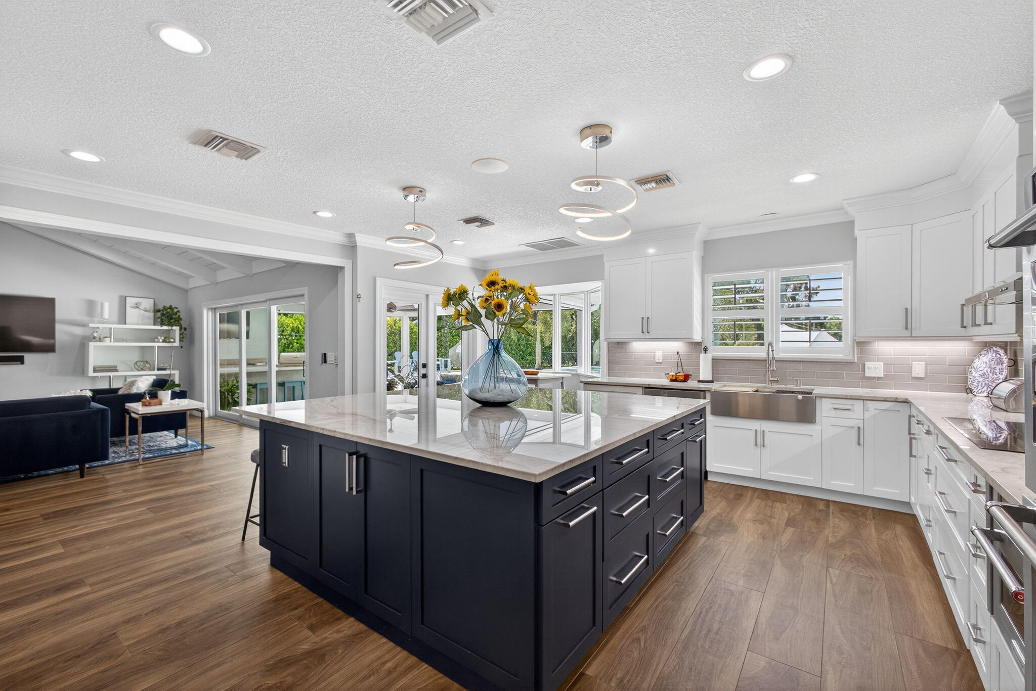 Kitchen featuring a contrasting oversized central island, white shaker-style cabinetry, stainless steel farmhouse sink, quartz countertops, and wood-finish flooring