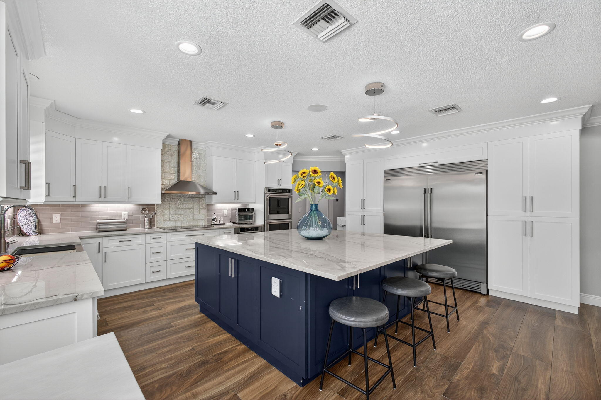 Kitchen featuring white cabinetry, a contrasting navy blue central island with stone countertop, wood-finish flooring, stainless steel appliances, and recessed lighting