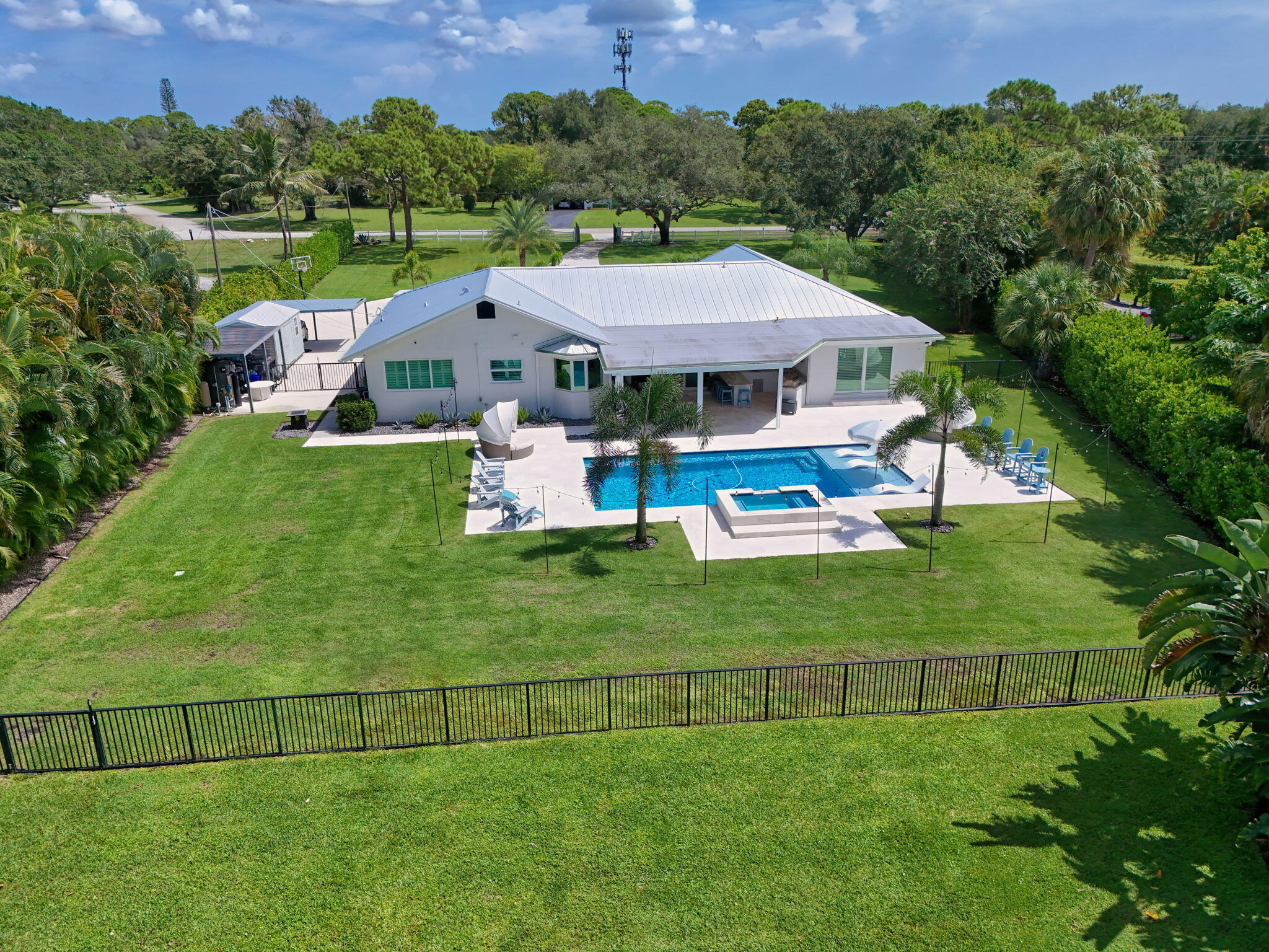 Single-story exterior featuring a metal roof, an in-ground swimming pool with an integrated spa, a paved pool deck, and a fenced backyard
