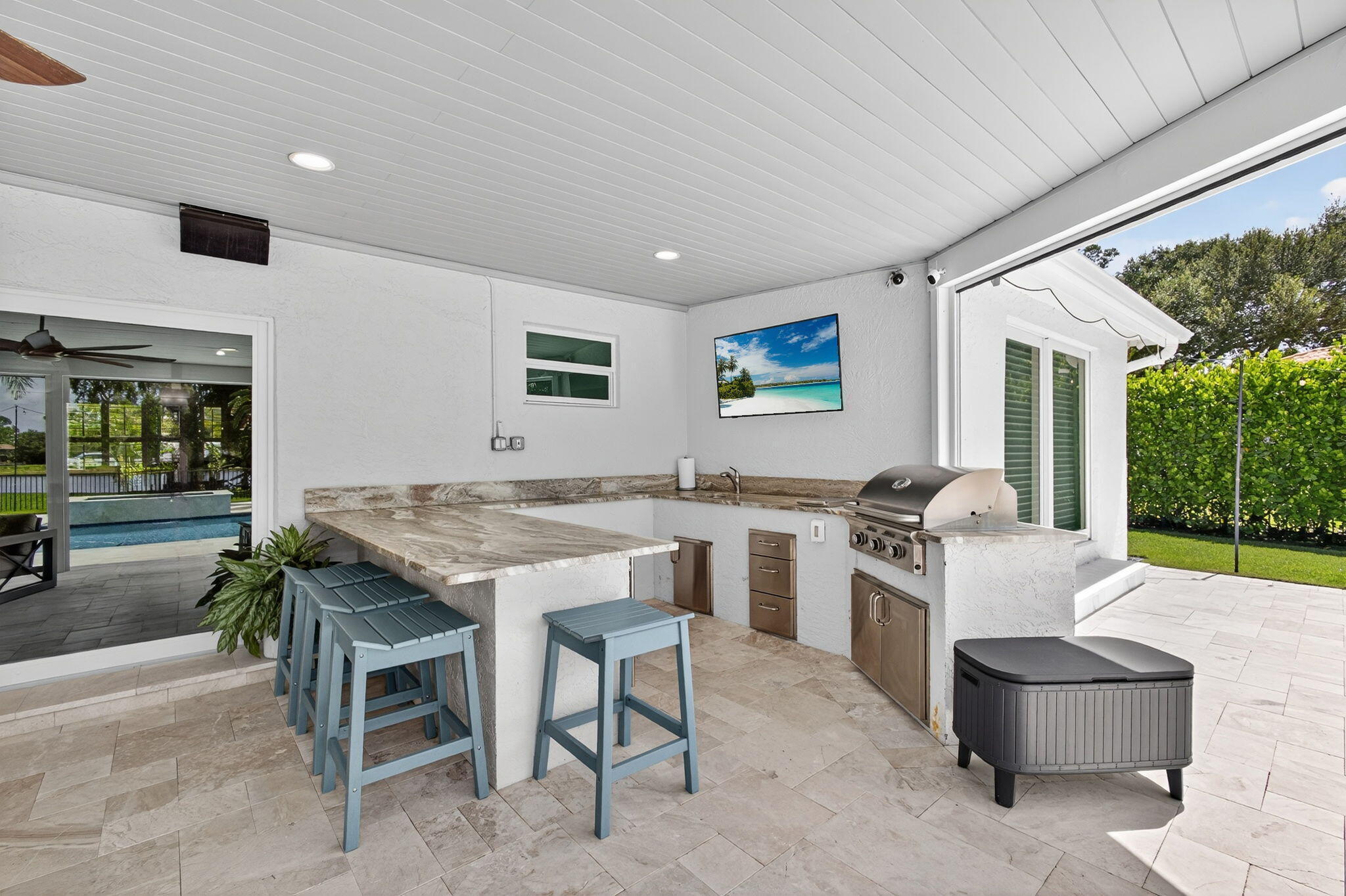 Covered outdoor kitchen featuring stone-finish countertops, built-in stainless steel grill, recessed lighting, and stone paver flooring