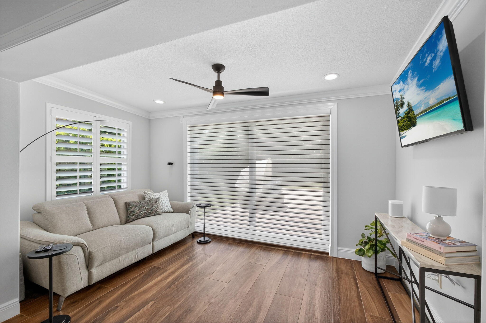 Wood-finish flooring, recessed lighting, matte black ceiling fan, plantation shutters, and light-filtering horizontal window shades