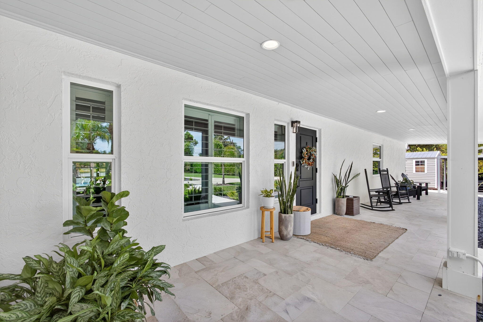 Covered front porch featuring large-format tile flooring, beadboard ceiling, recessed lighting, and a dark-toned entry door