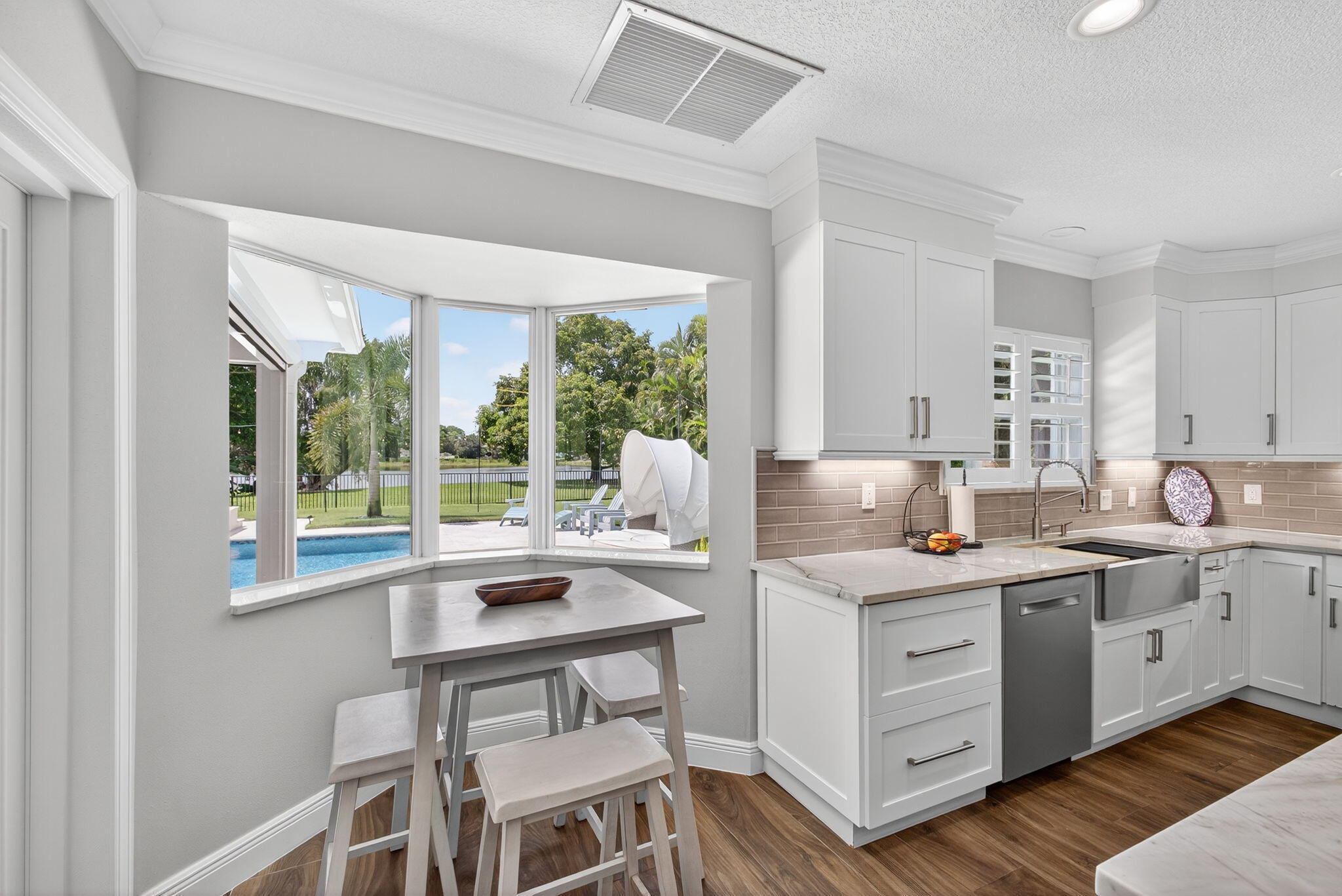 Kitchen featuring white shaker-style cabinetry, stone-surface countertops, horizontal tile backsplash, stainless steel apron-front sink, and bay window