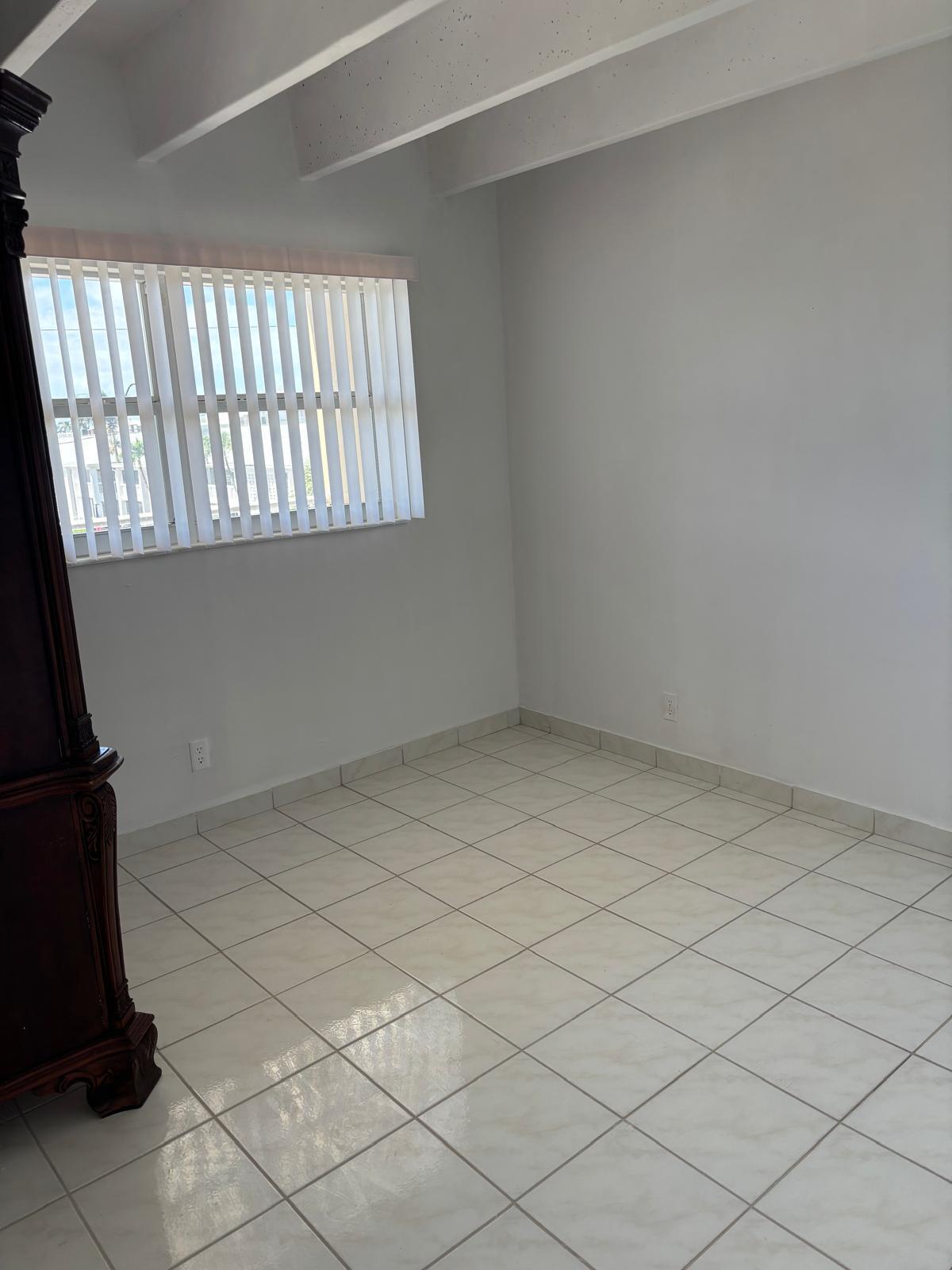 Room featuring neutral tile flooring, exposed ceiling beams, and vertical window blinds