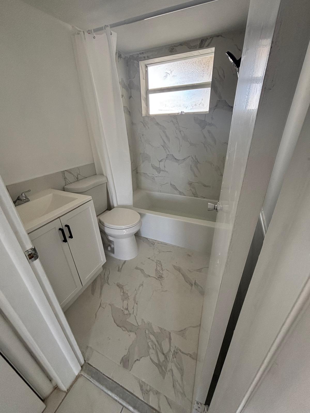 Bathroom featuring stone-finish wall tile, white vanity cabinet with black hardware, integrated sink, and stone-finish floor tile