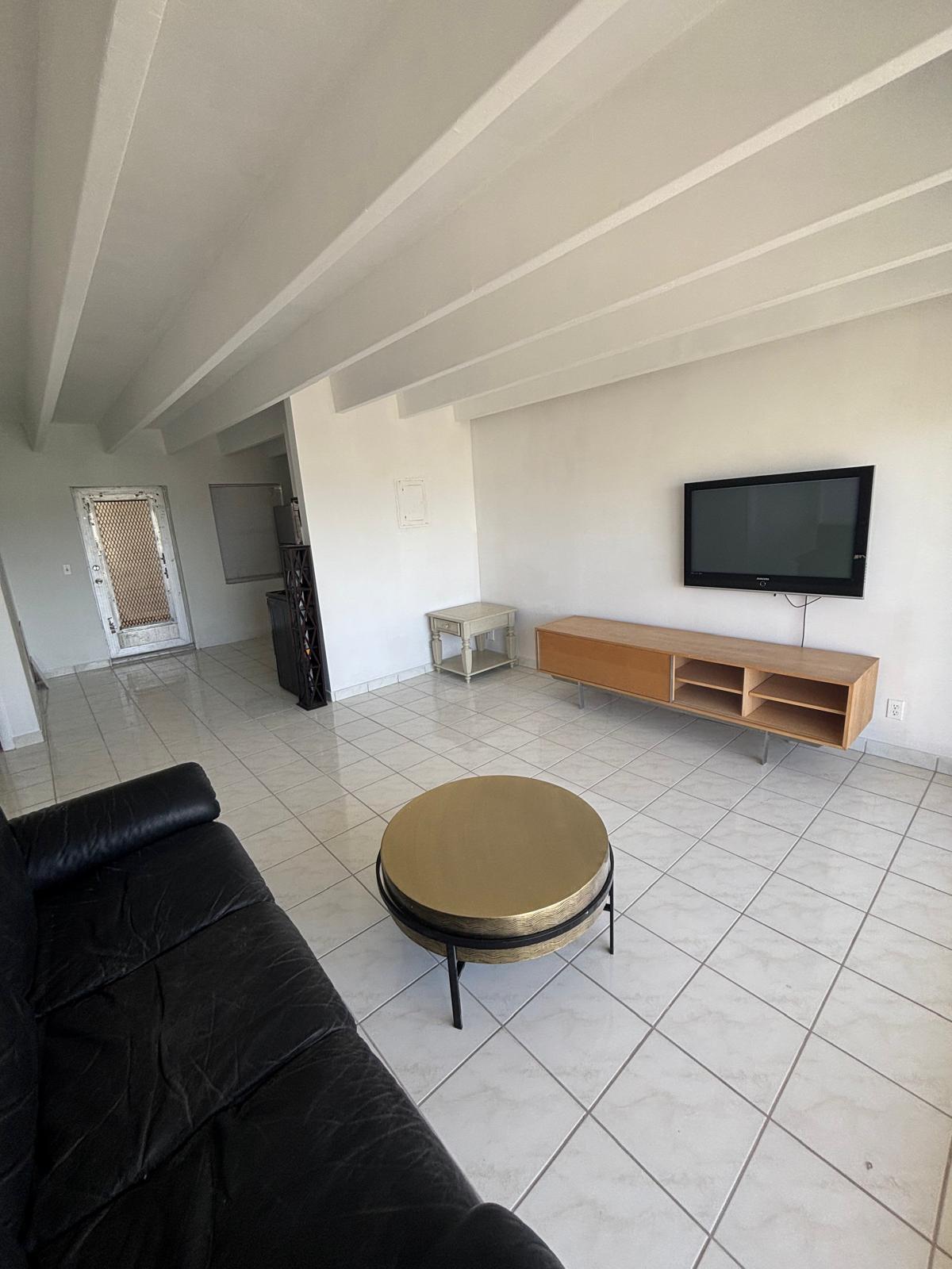 Open-concept space featuring high exposed-beam ceilings, polished ceramic tile flooring, and a mounted media cabinet