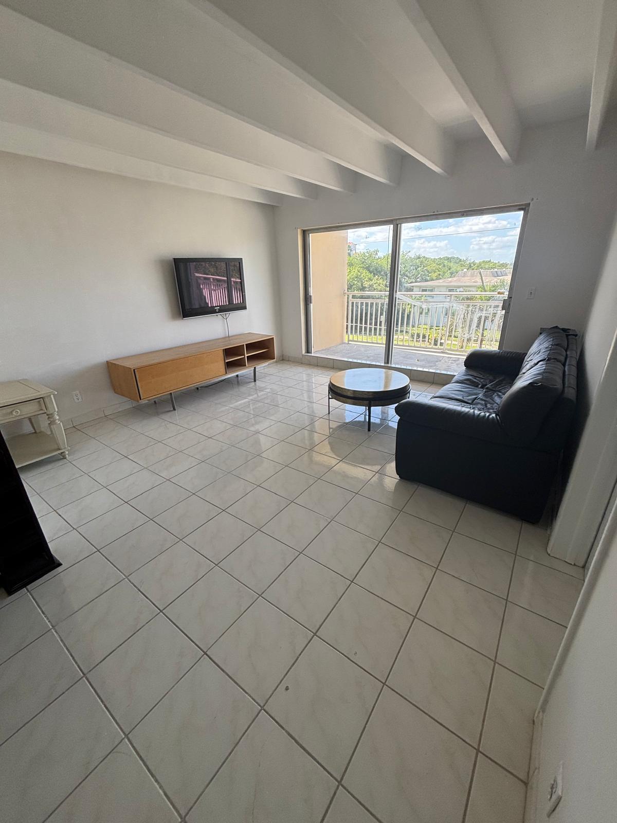 Living area featuring a vaulted ceiling with exposed beams, ceramic tile flooring, and a sliding glass door providing external access