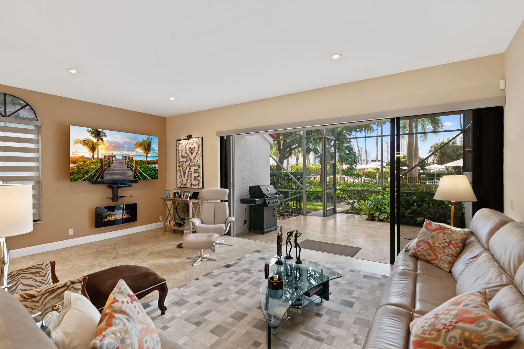 Living area featuring large-format tile flooring, recessed lighting, wall-mounted electric fireplace, and expansive multi-panel sliding glass doors opening to a screened-in lanai