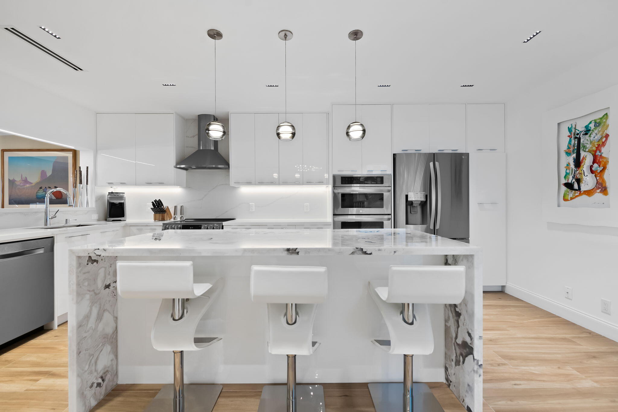 Kitchen featuring a waterfall-edge stone island, high-gloss cabinetry, stainless steel appliances, recessed ceiling lighting, and wood-finish flooring