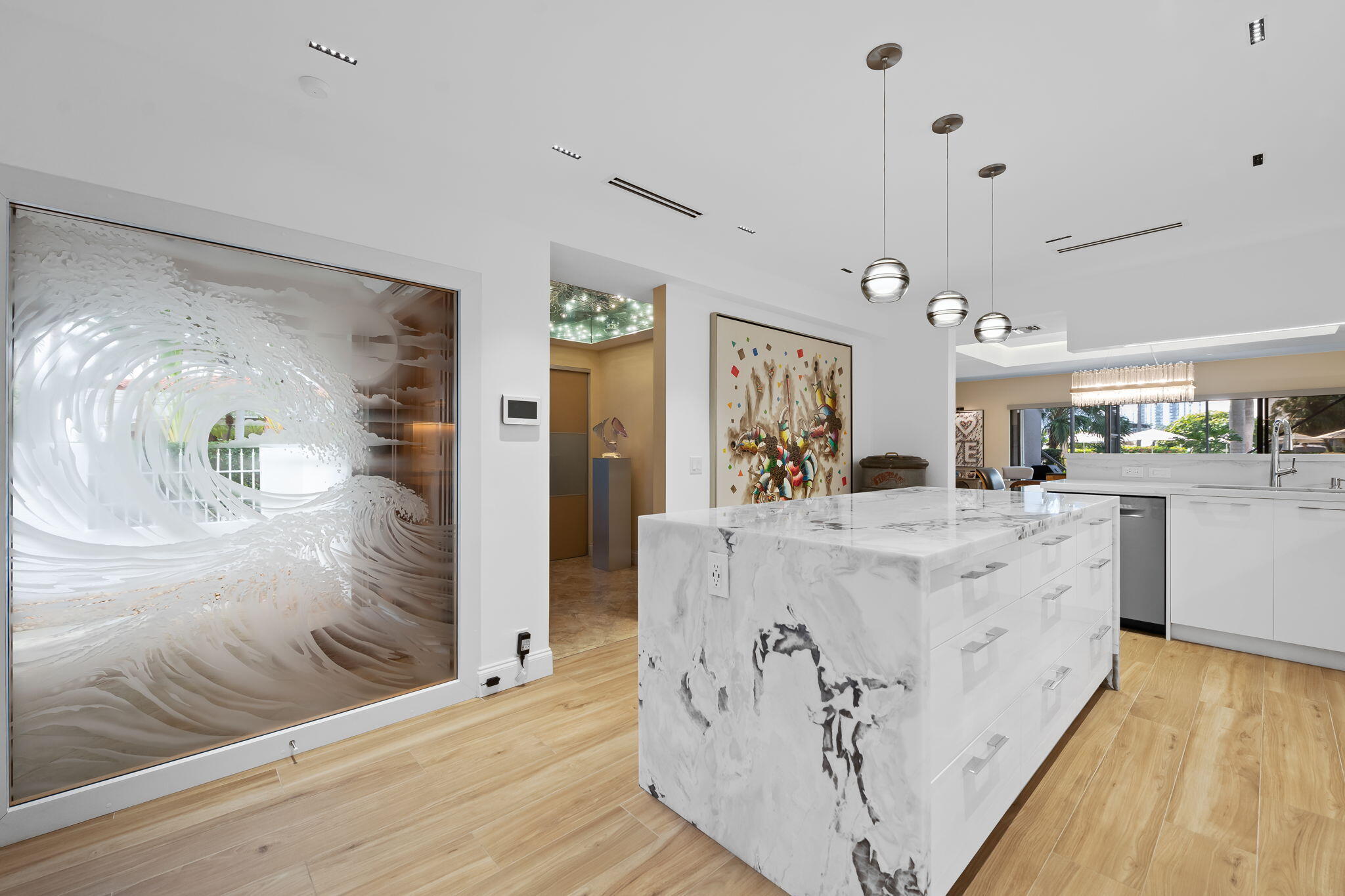 Kitchen featuring a large central island with natural stone waterfall countertops, wood-finish flooring, custom pendant lighting, and a decorative glass feature wall