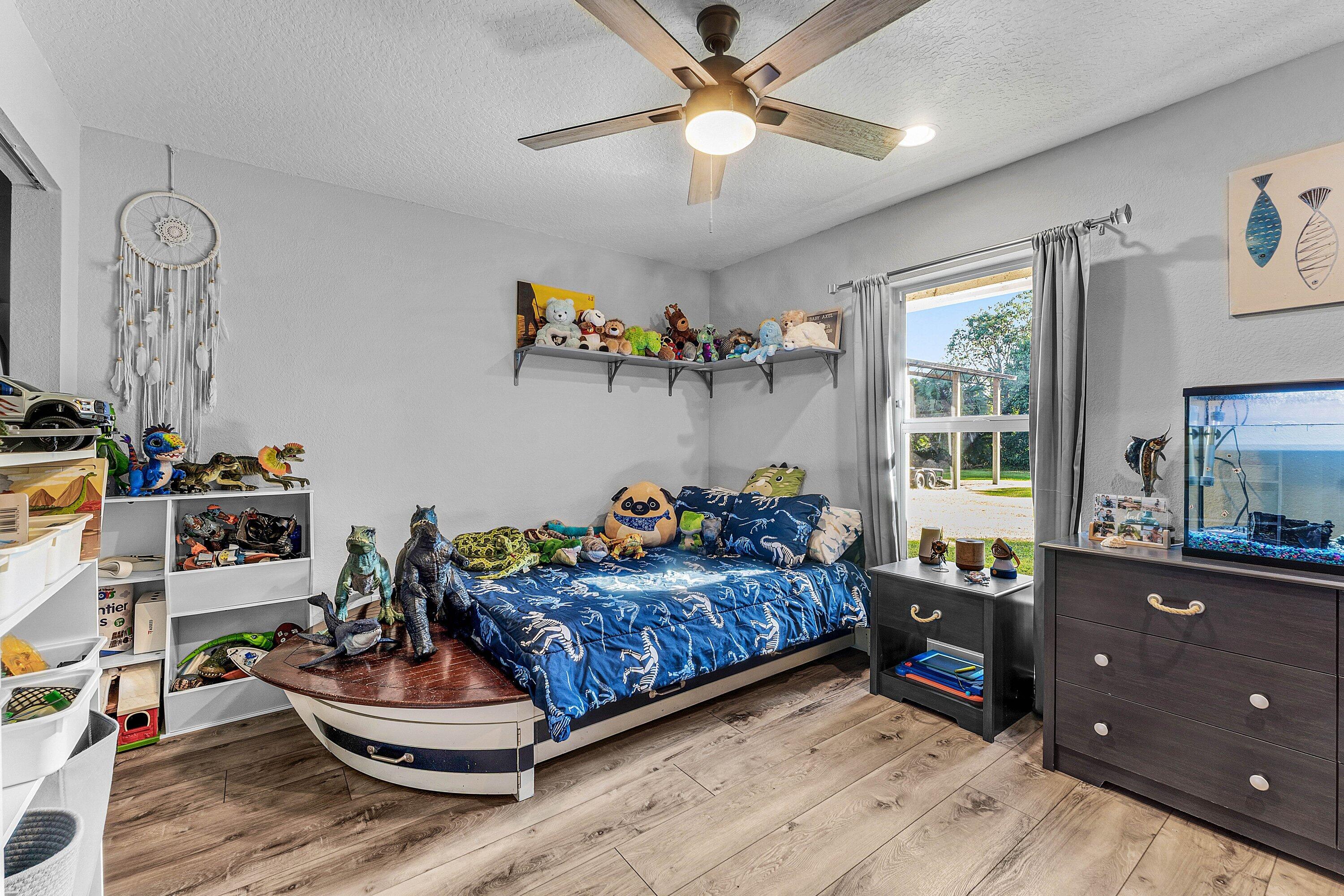 Neutral-toned interior featuring wood-finish flooring, a ceiling fan with integrated lighting, and a single-hung window with curtain rod hardware