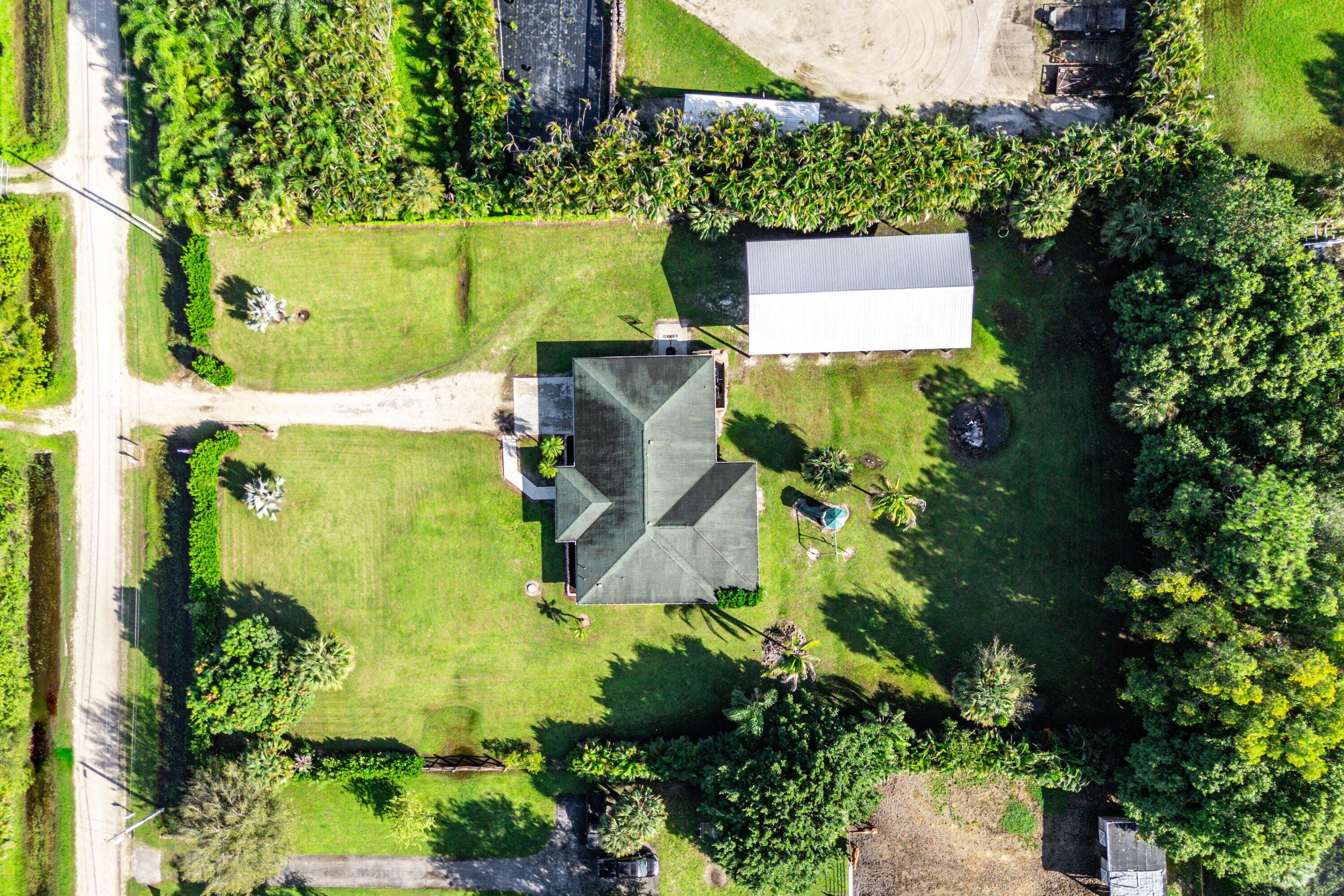 Aerial view of a sprawling property featuring an expansive lawn, detached metal-roofed structure, and mature perimeter trees
